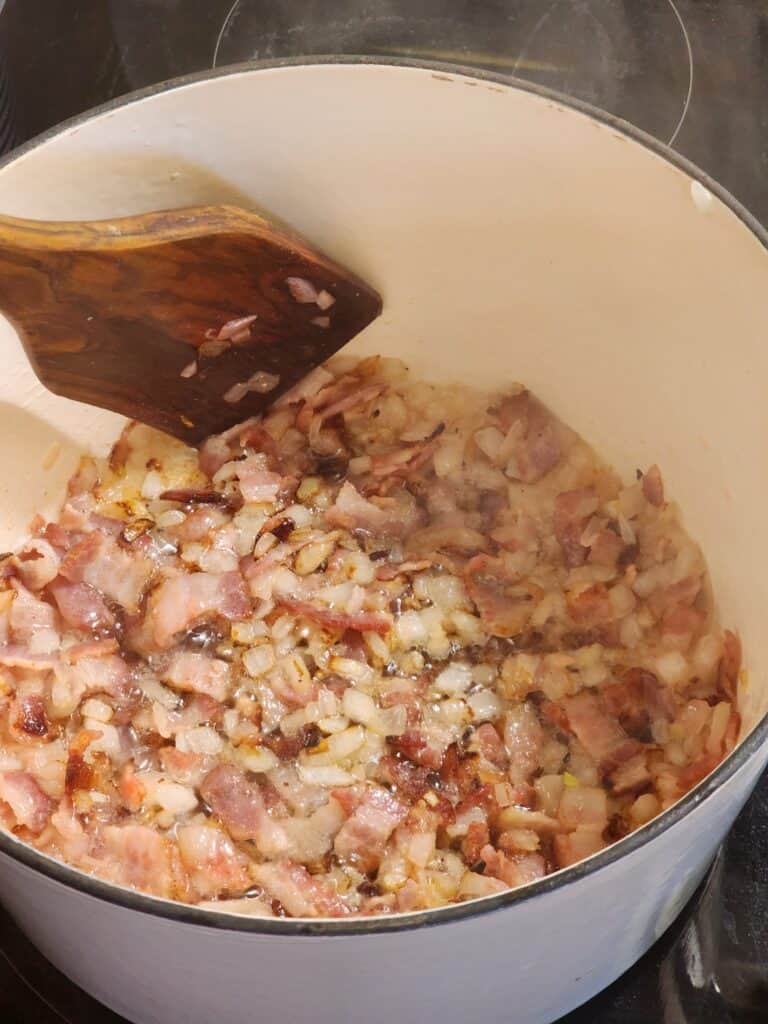 bacon and onions being sauteed in a dutch oven