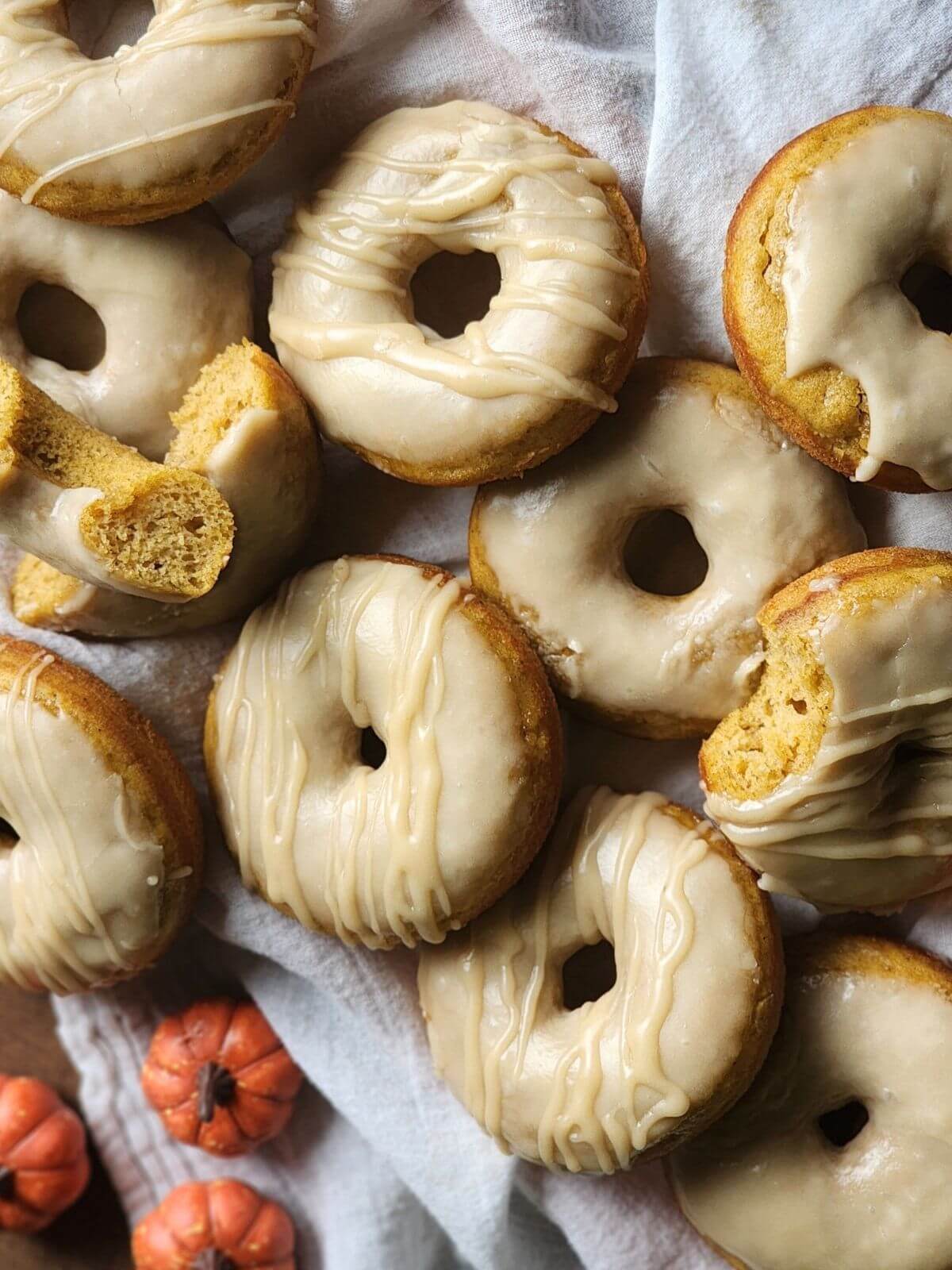 Baked pumpkin donuts with maple glaze and a maple drizzle arranged on a linen cloth.