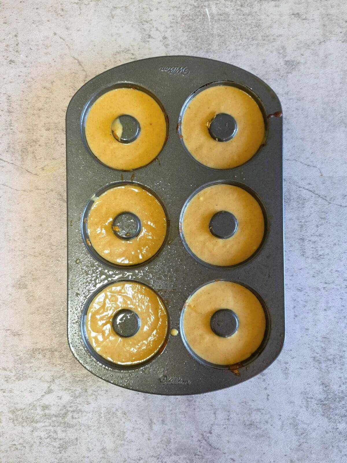 Pumpkin donut batter divided in a greased donut pan.