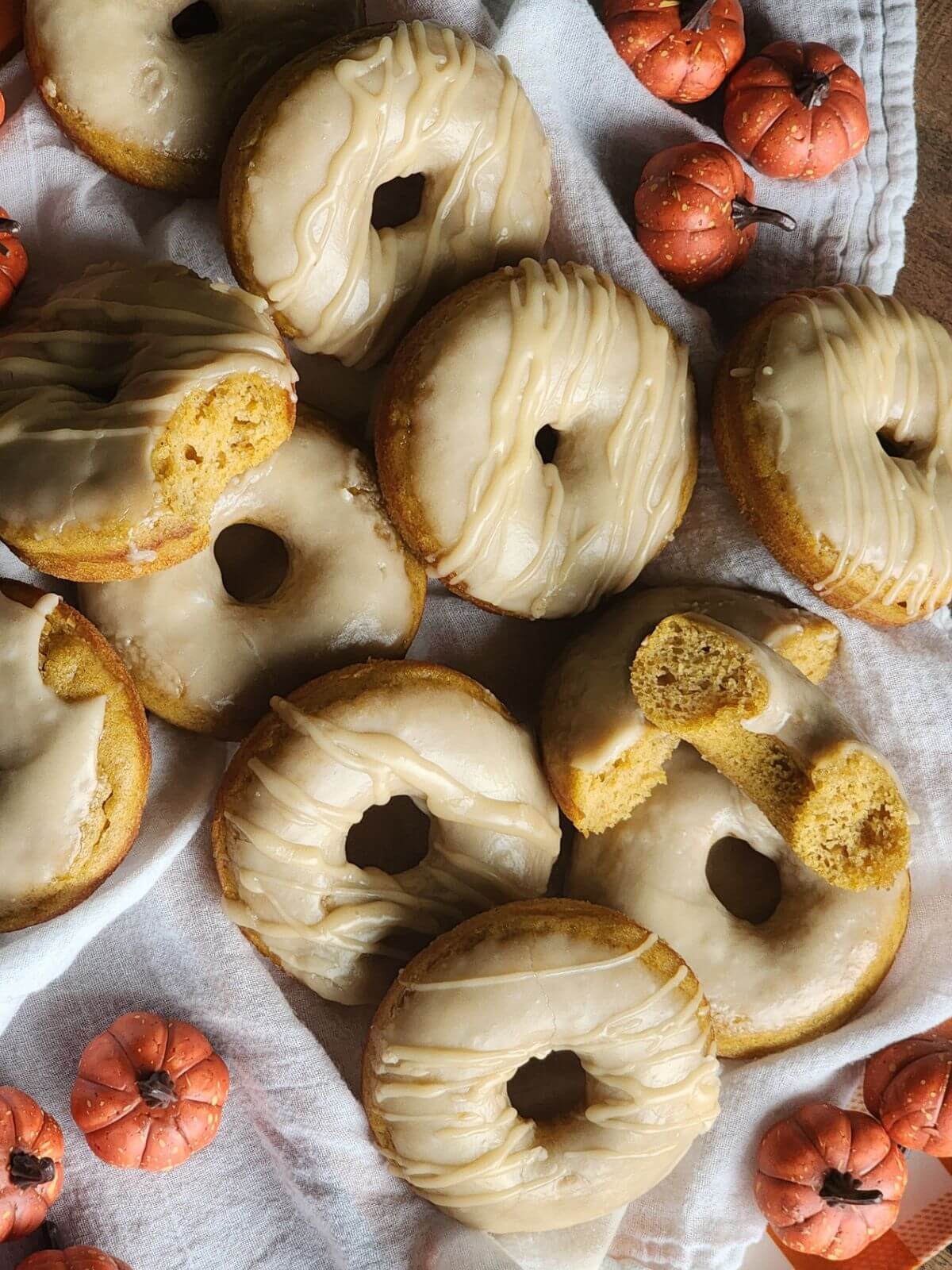 Maple glazed pumpkin donuts arranged with small decorative pumpkins.