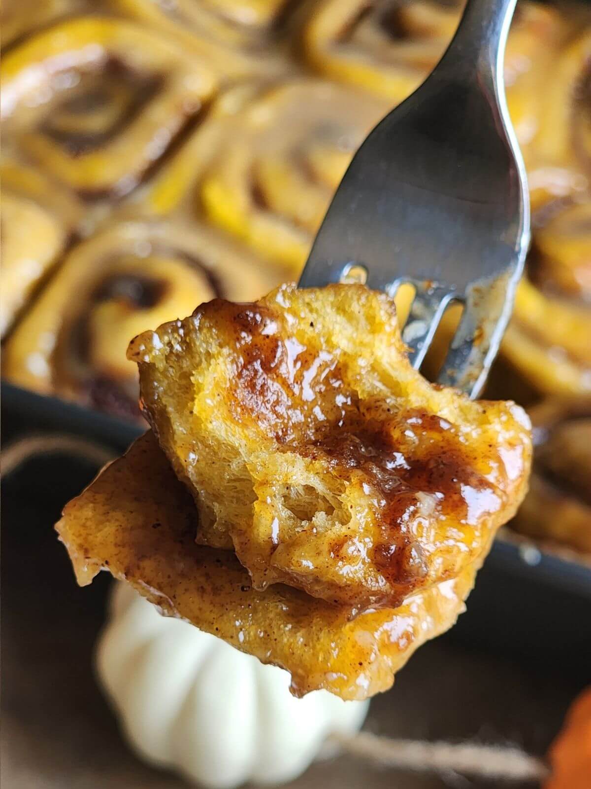 Soft sourdough pumpkin cinnamon roll with cinnamon filling and caramel glaze on a fork.