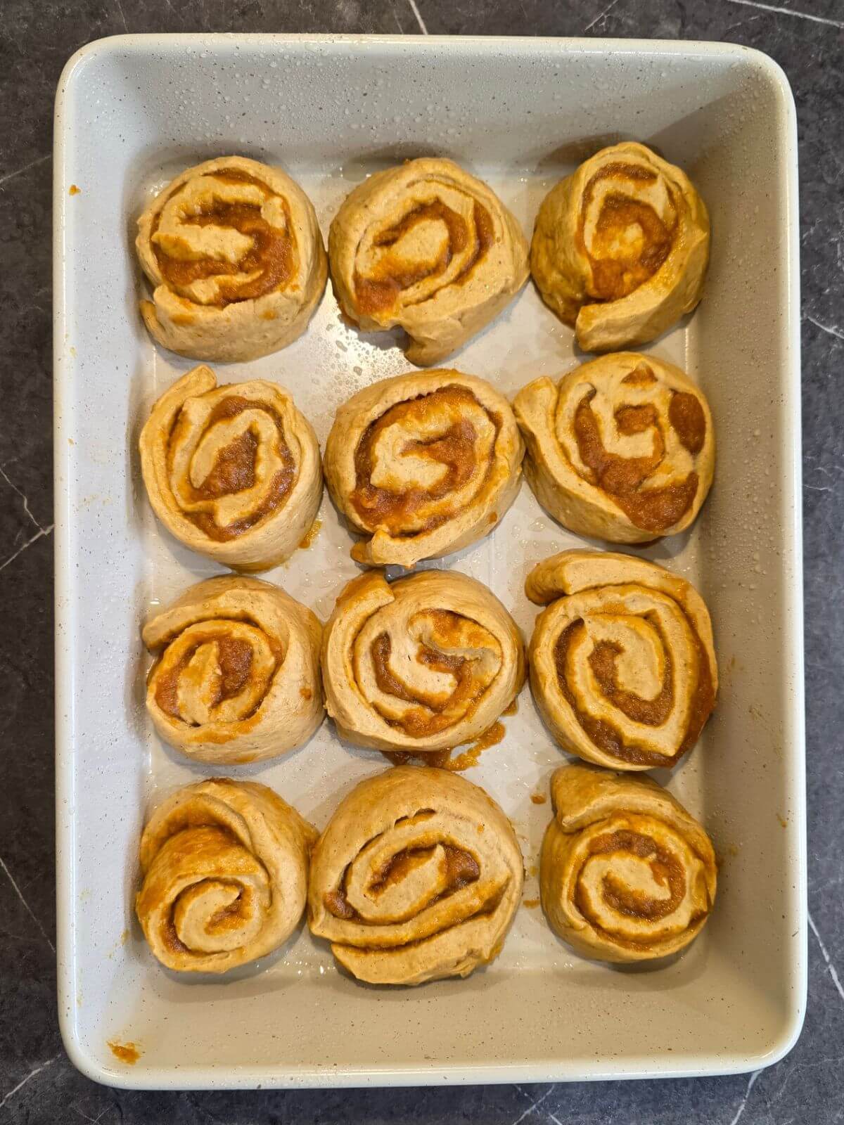 Sliced sourdough pumpkin cinnamon rolls arranged in a baking dish before the final rise.