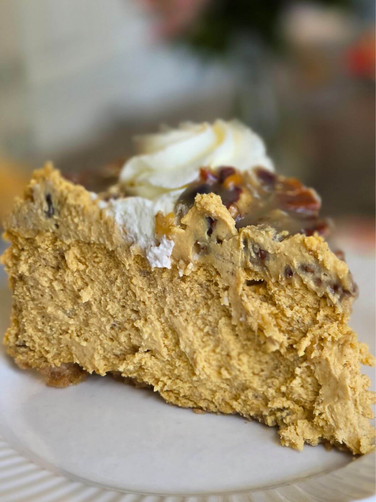 Slice of pumpkin cheesecake with caramel pecan topping and whipped cream on a plate.