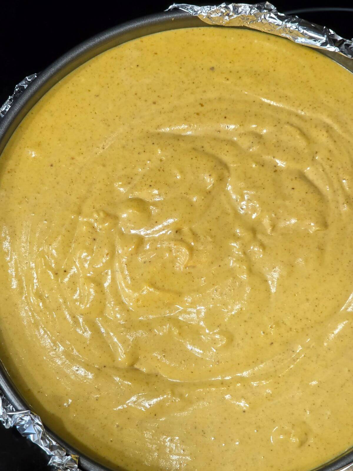 Pumpkin cheesecake batter smoothed into a foil wrapped springform pan before baking.