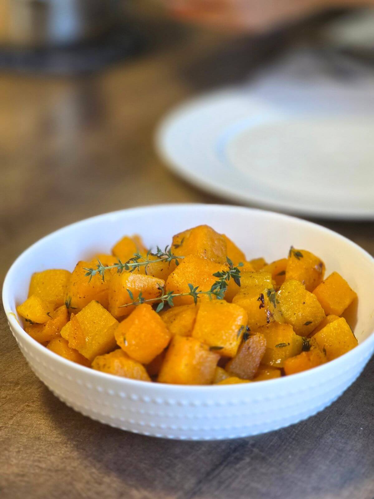 Roasted butternut squash cubes served in a white bowl with fresh thyme.