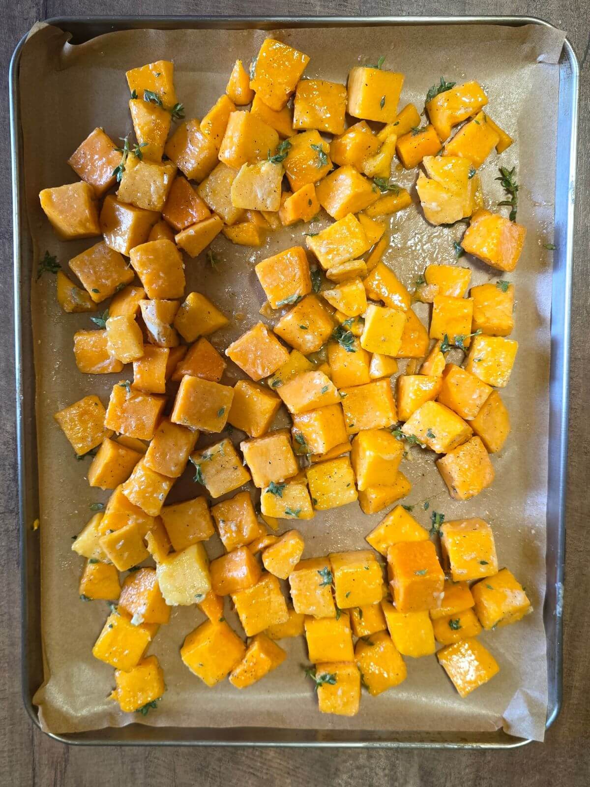 Roasted butternut squash cubes spread on a parchment lined baking sheet.