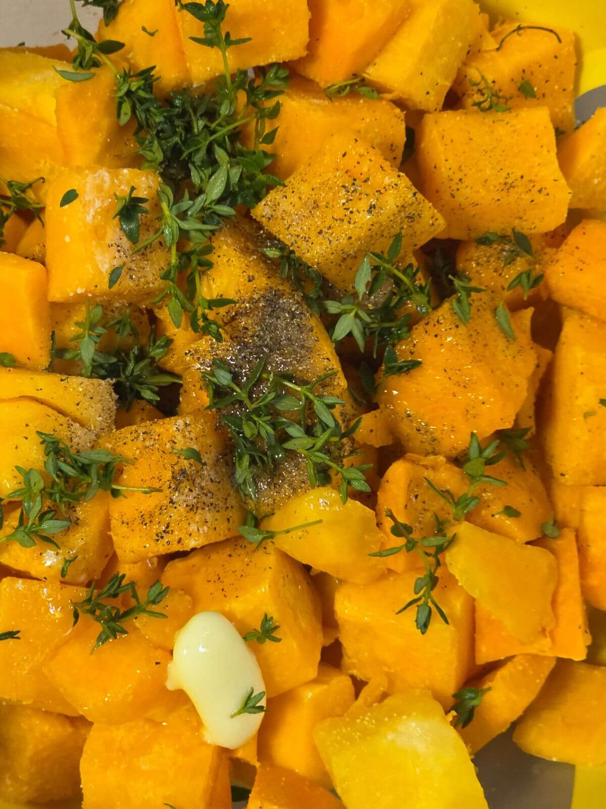 Butternut squash cubes tossed with butter, maple syrup, thyme, salt, and pepper before roasting.