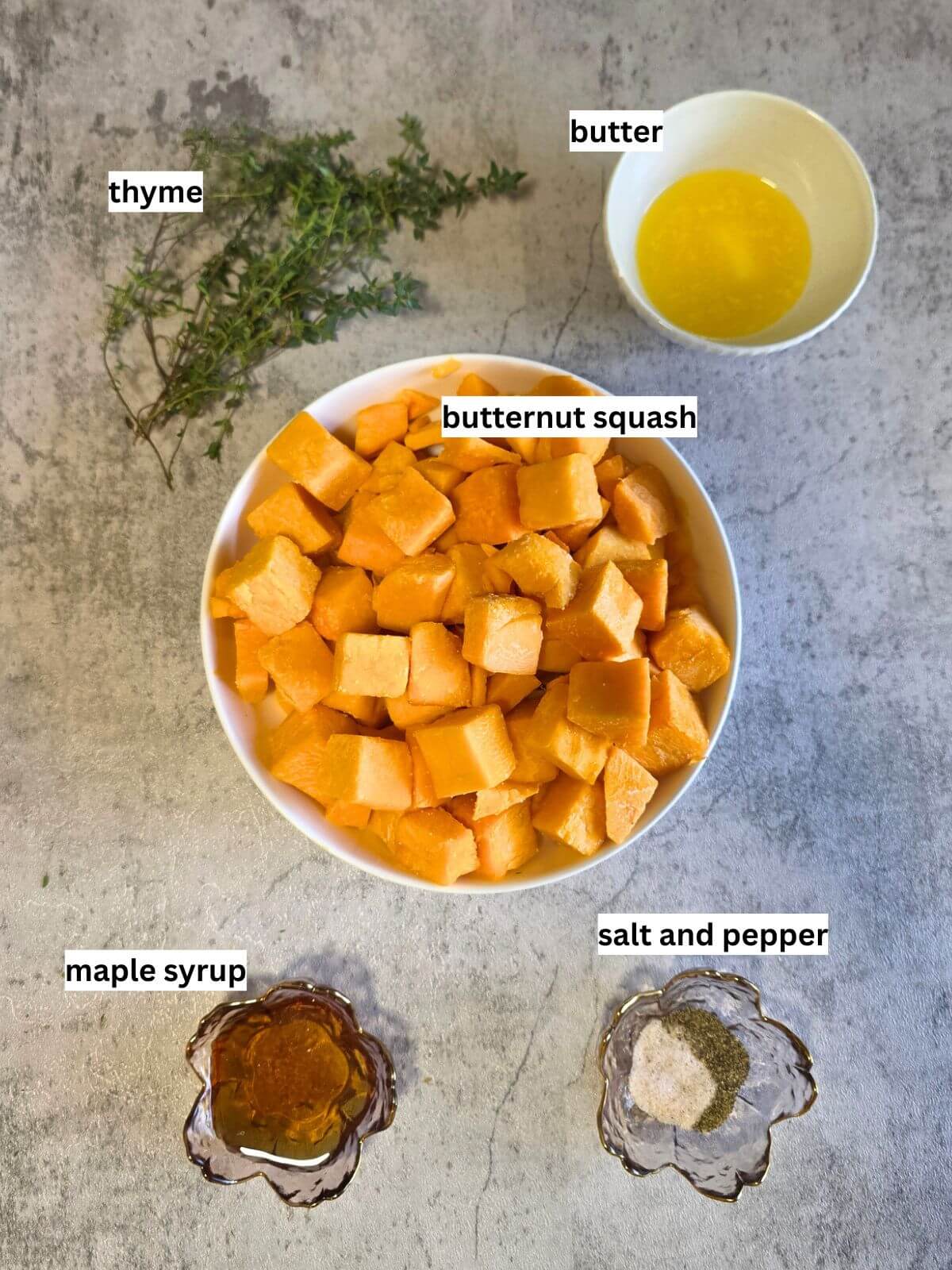 Ingredients for roasted butternut squash cubes including squash, butter, maple syrup, thyme, salt, and pepper.