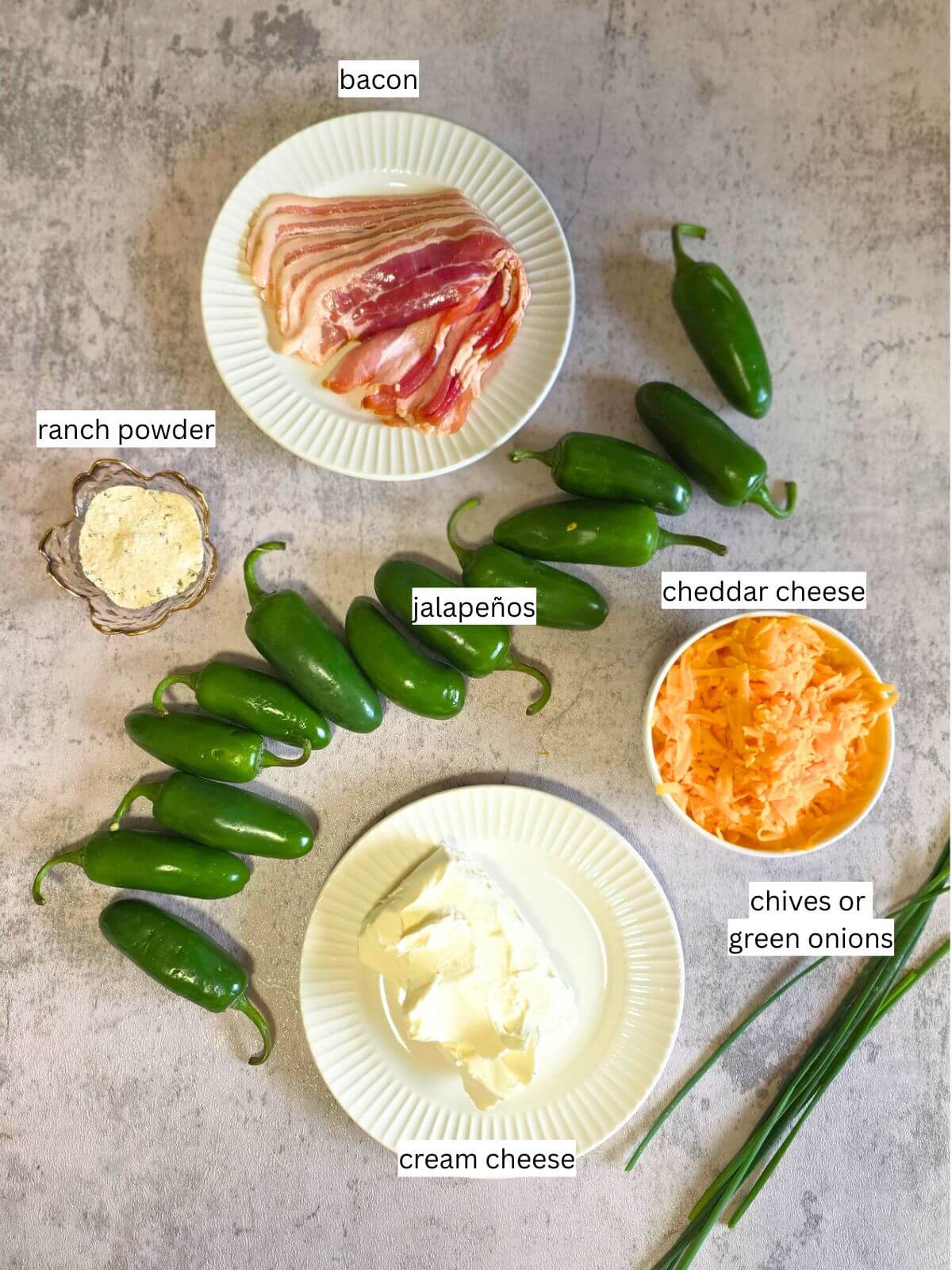 Ingredients for cream cheese jalapeño poppers including jalapeños, bacon, cheddar cheese, cream cheese, ranch seasoning, and chives.