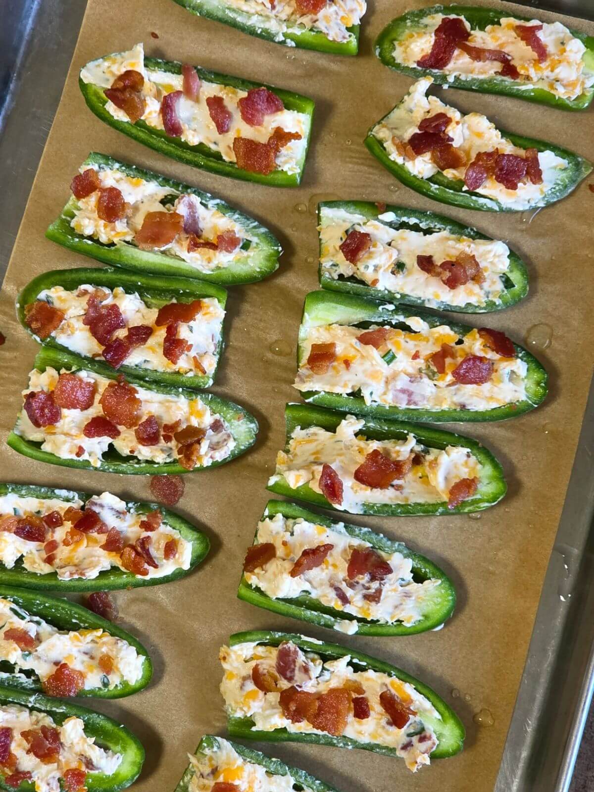 Jalapeño halves stuffed with cream cheese filling and topped with bacon before baking.