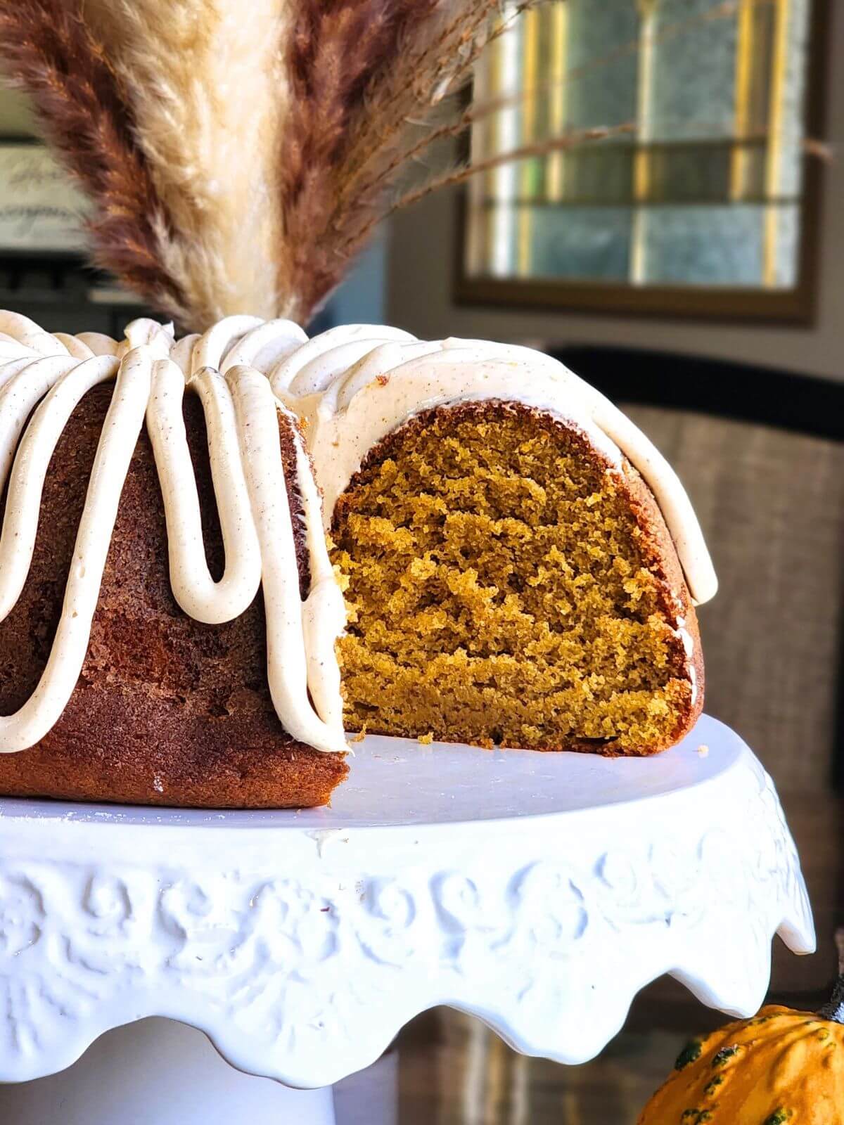 Sliced pumpkin spice Bundt cake with cream cheese frosting on a white cake stand.