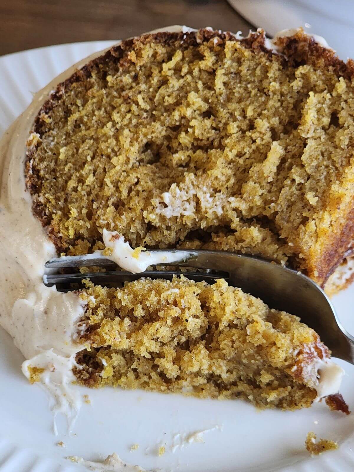 Close up of a moist slice of pumpkin spice Bundt cake with cream cheese frosting on a plate.