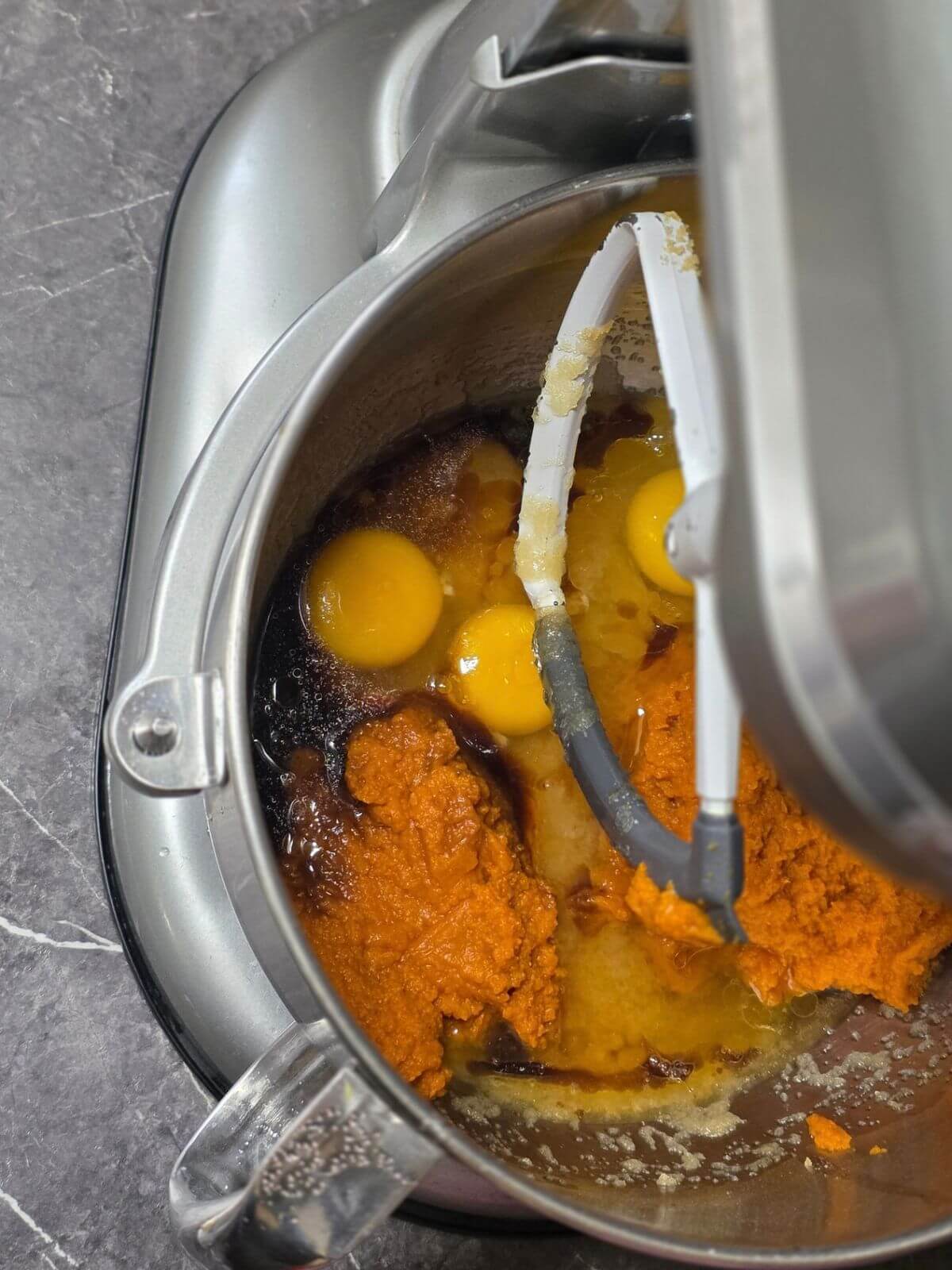 Pumpkin puree, eggs, vanilla, and other wet ingredients added to a stand mixer bowl.