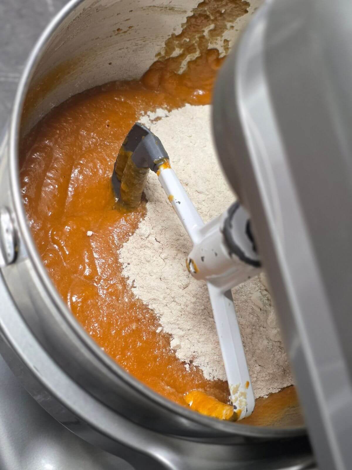 Dry ingredients being added to the pumpkin mixture in a stand mixer.