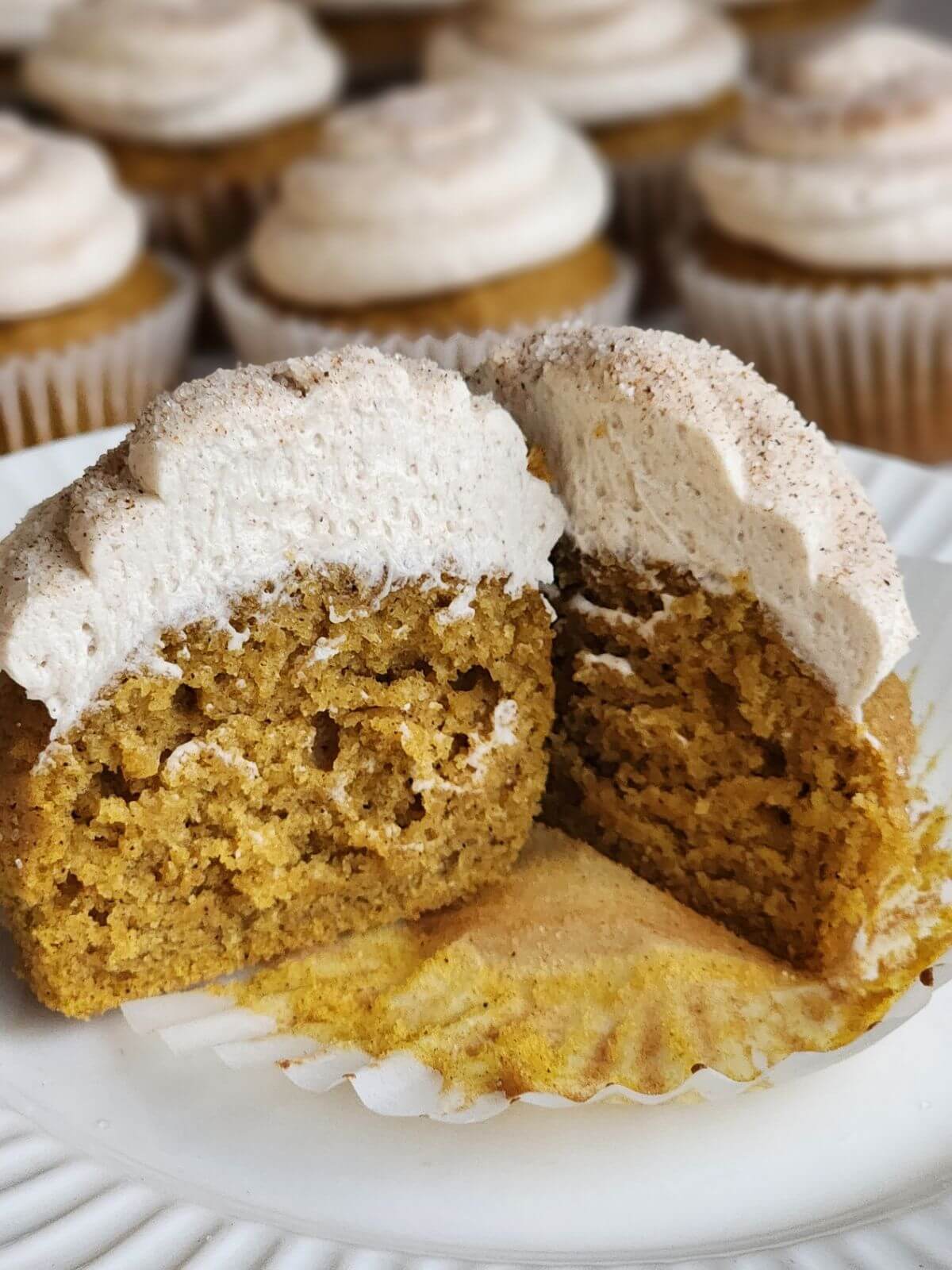 Cut pumpkin spice cupcake topped with cinnamon buttercream, showing the soft pumpkin crumb inside.