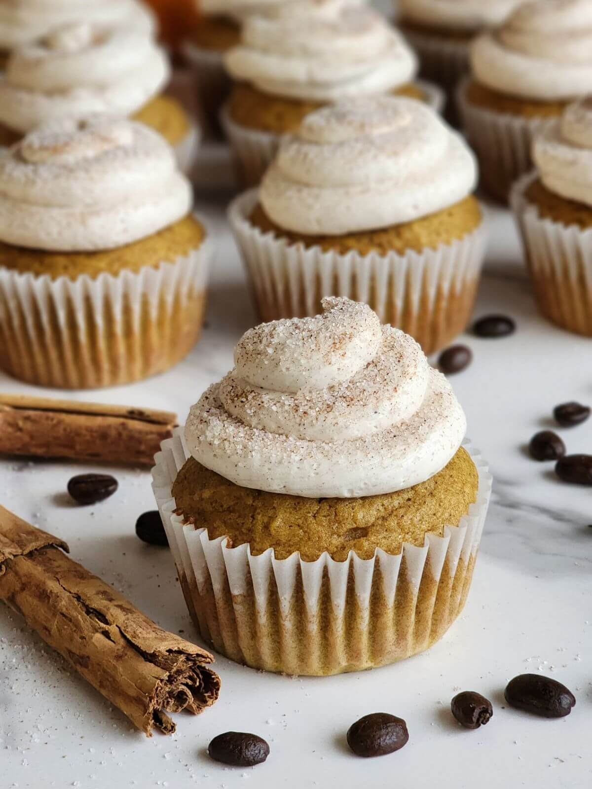 Pumpkin spice cupcakes with cinnamon buttercream, cinnamon sticks, and scattered coffee beans.