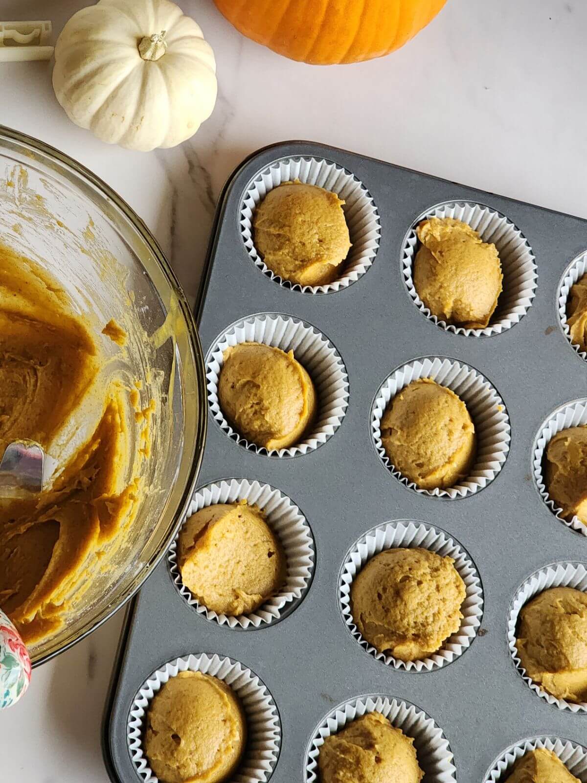 Pumpkin cupcake batter portioned into paper liners in a muffin pan.