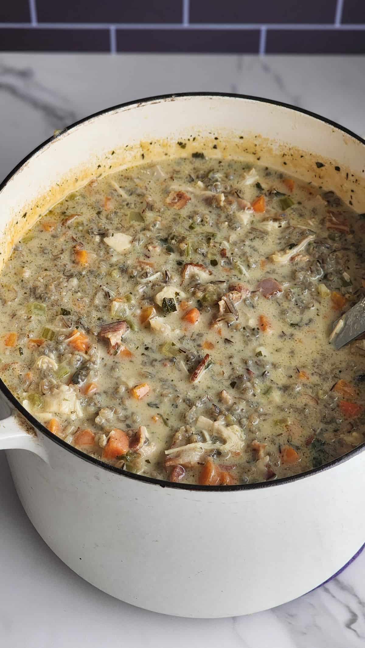 A pot of creamy chicken wild rice soup with tender chicken, vegetables, and herbs.