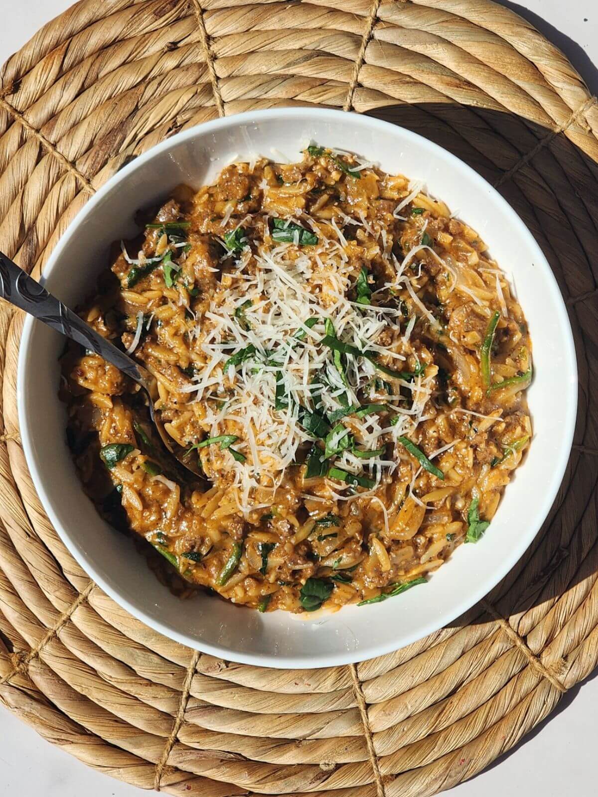 Ground beef orzo recipe with creamy tomato sauce served in a white bowl with parmesan cheese and fresh basil on top.