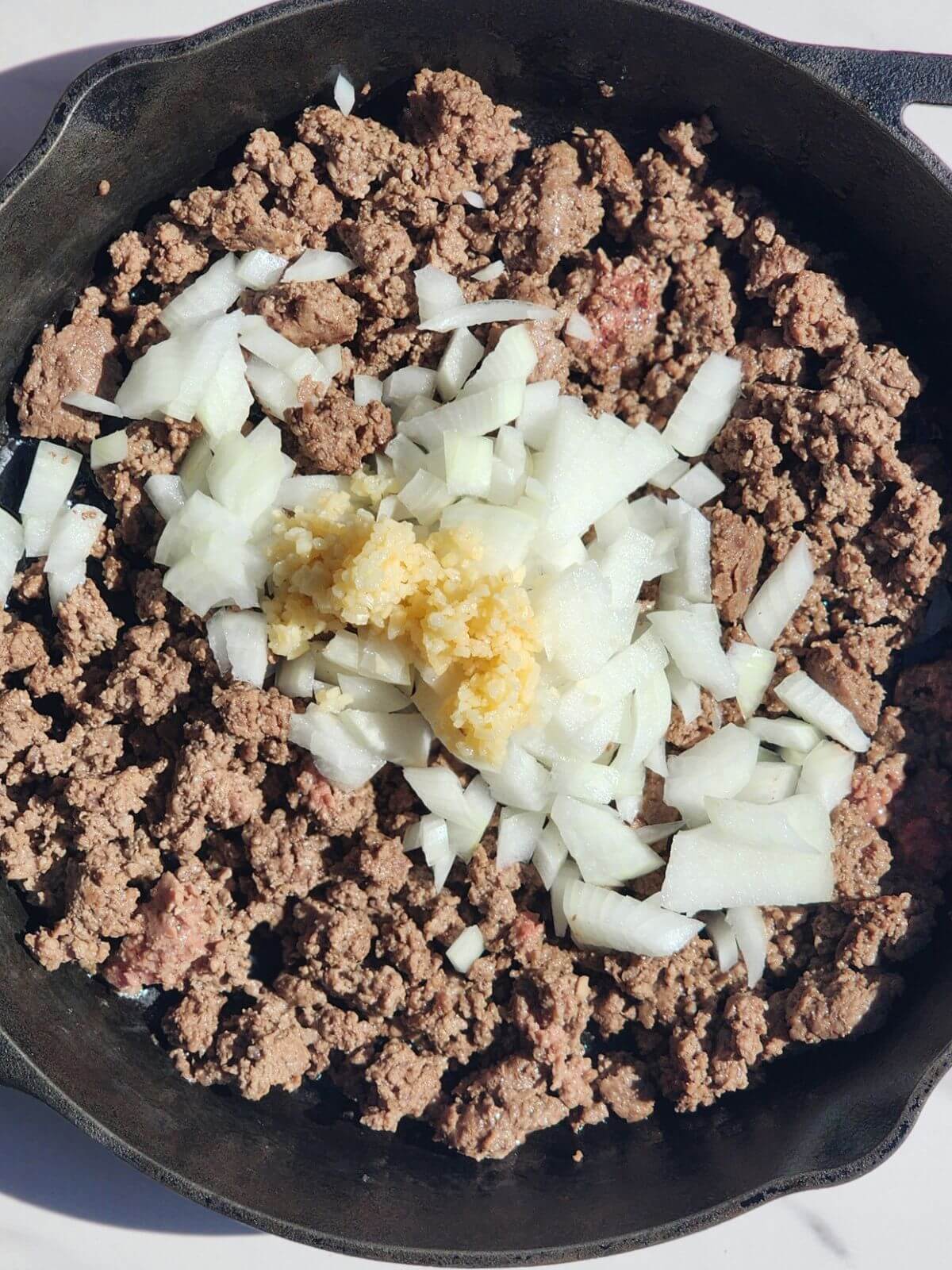 Ground beef cooked in a cast iron skillet with diced onion and minced garlic.