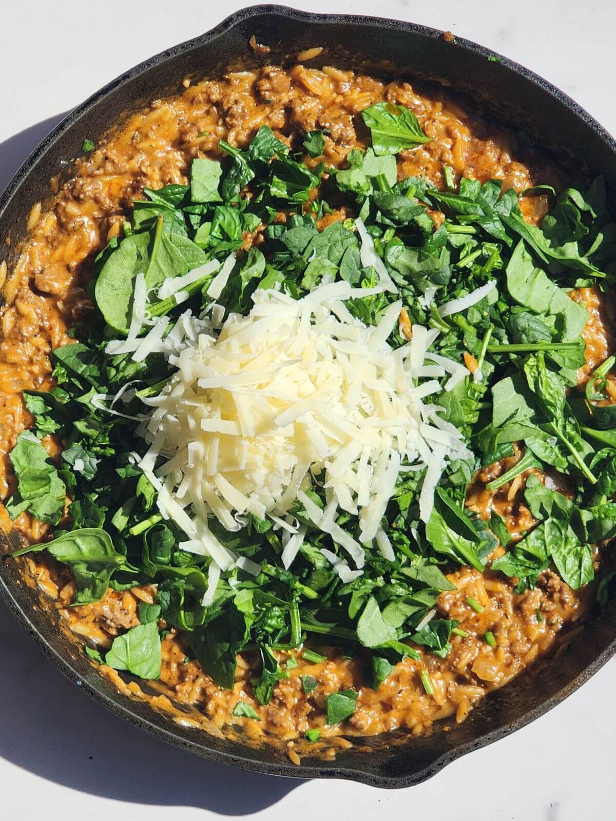 Spinach and parmesan cheese added to creamy ground beef orzo in a cast iron skillet.