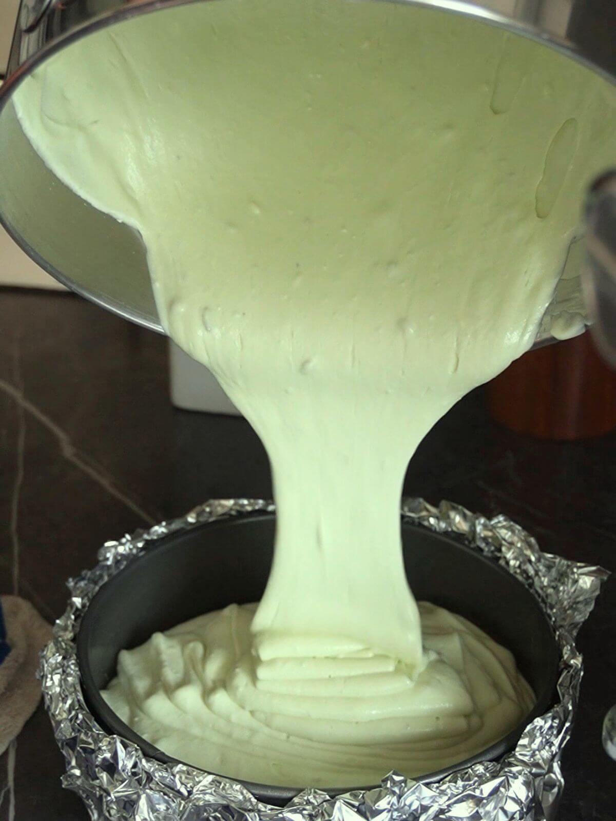 Pistachio cheesecake batter being poured into a foil wrapped springform pan.