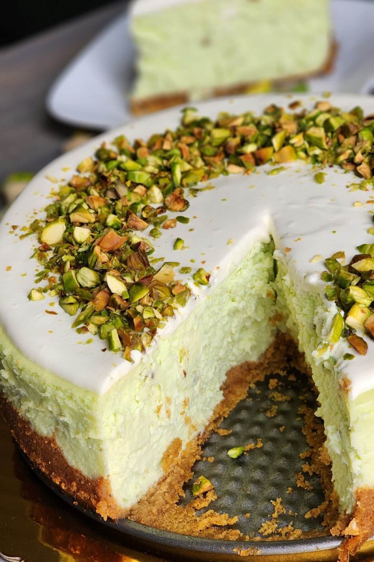 Pistachio cheesecake with sour cream icing, chopped pistachios, and a slice removed.