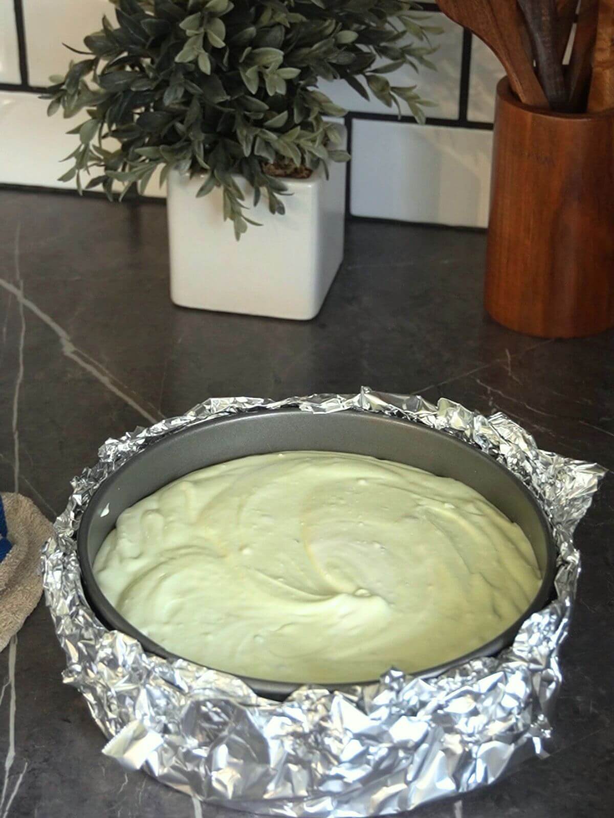 Smooth pistachio cheesecake filling in a foil wrapped springform pan before baking.