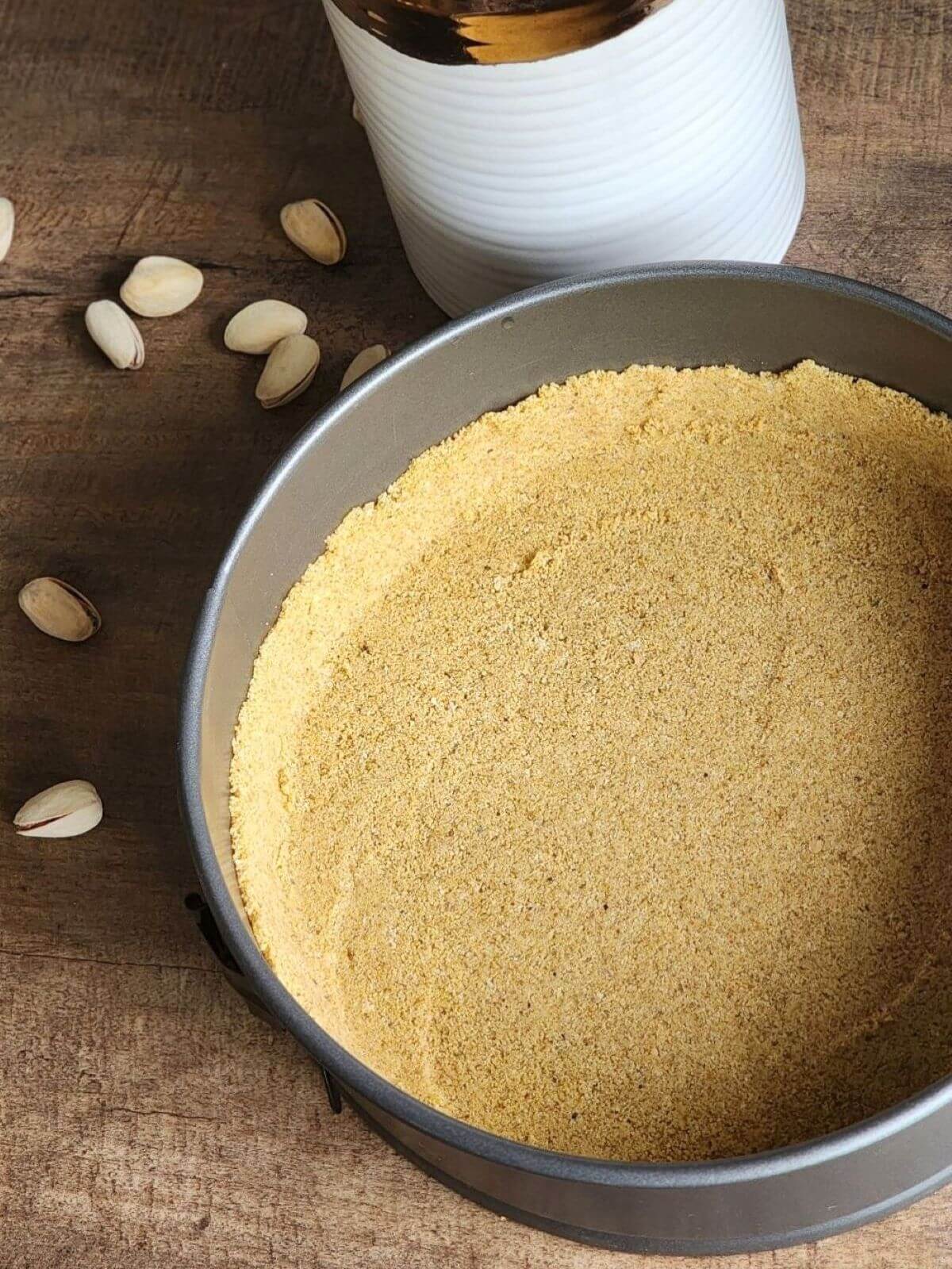 Graham cracker crust pressed into a springform pan for pistachio cheesecake.