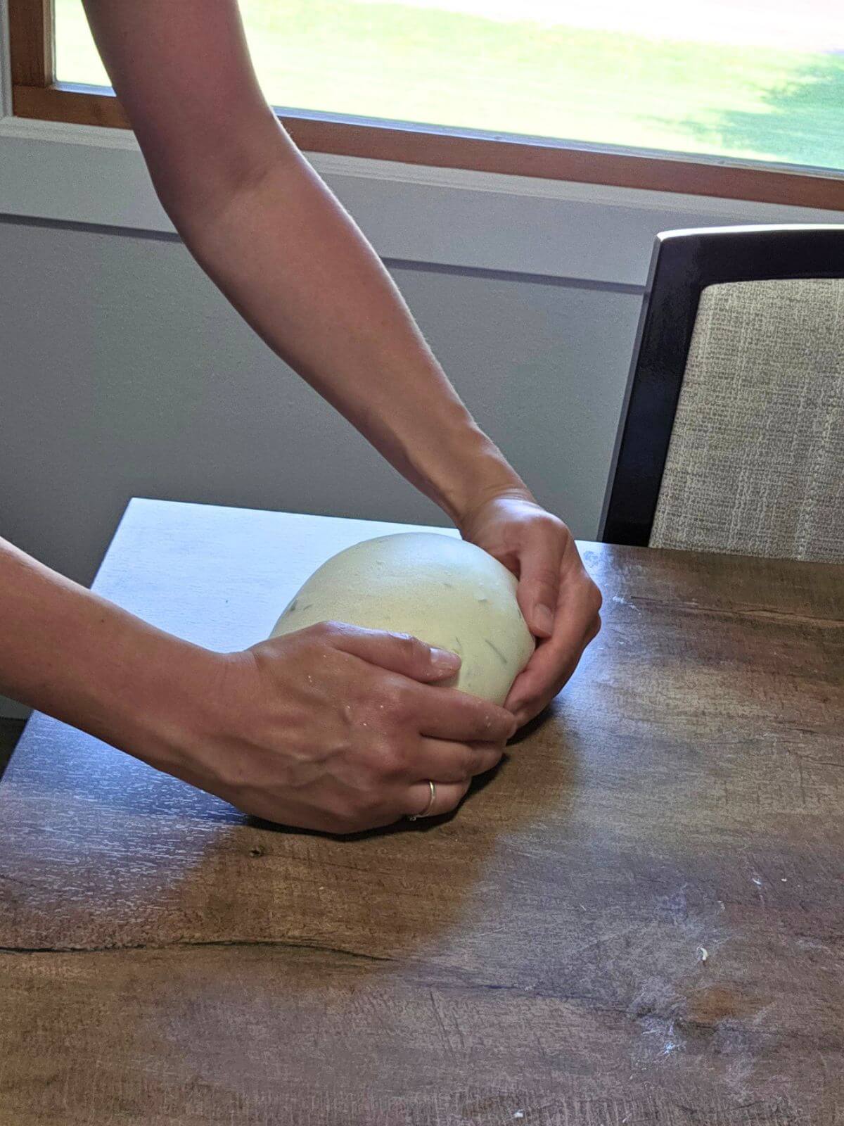 Hands shaping roasted garlic and rosemary sourdough bread dough on a wooden table.