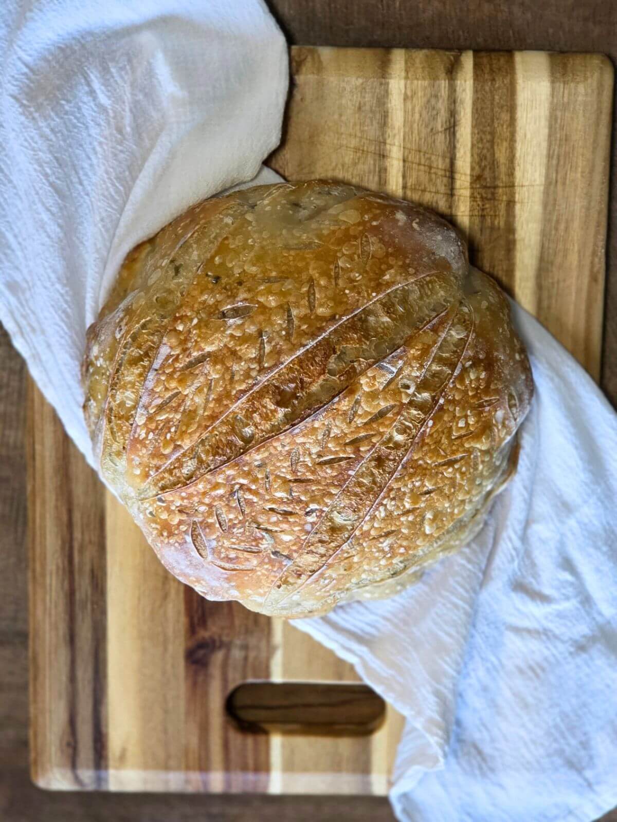 Freshly baked roasted garlic and rosemary sourdough bread cooling on a cutting board.