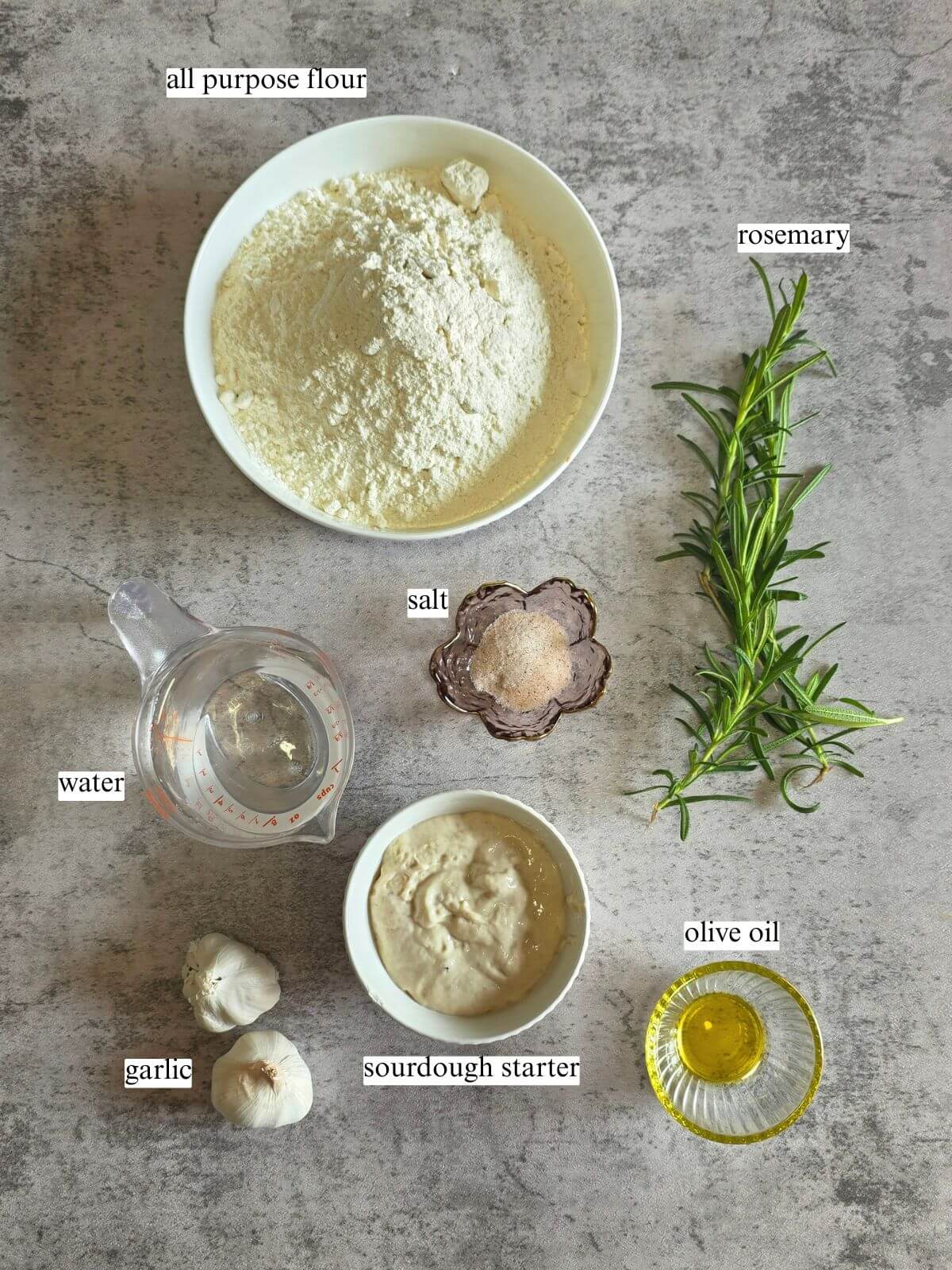 Ingredients for roasted garlic and rosemary sourdough bread including sourdough starter, flour, roasted garlic, fresh rosemary, water, and salt.