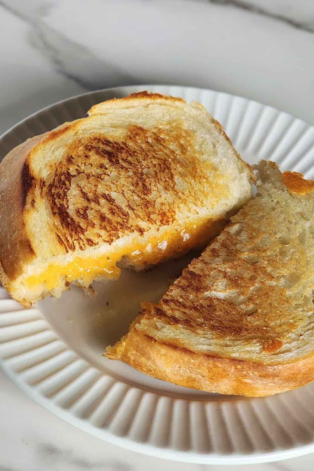 Grilled cheese sandwich on a plate, cut in half.