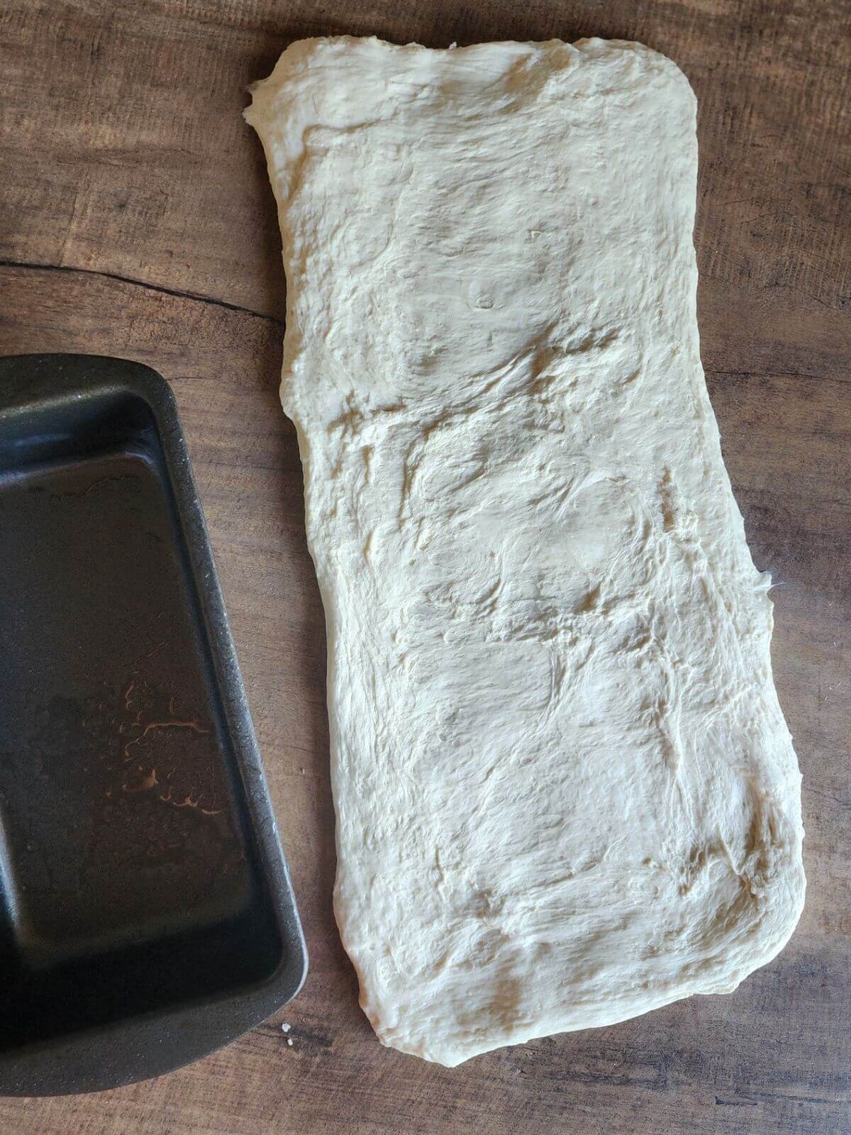 Dough rolled into a rectangle with bread pan beside it.