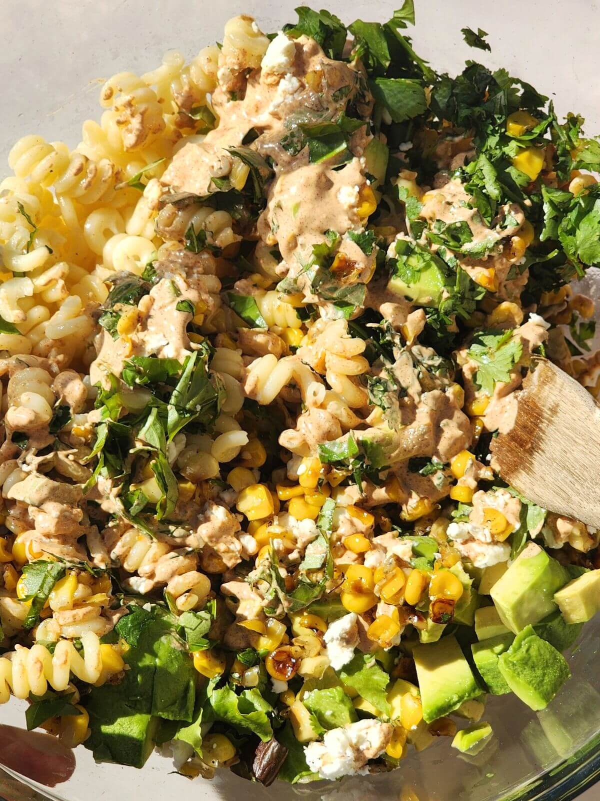 Mexican street corn pasta salad being tossed with creamy chili lime dressing, avocado, corn, cotija cheese, and herbs.