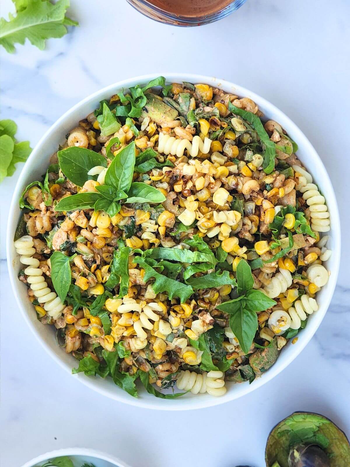 Mexican street corn pasta salad with avocado, cotija cheese, corn, fresh herbs, and creamy chili lime dressing served in a bowl.