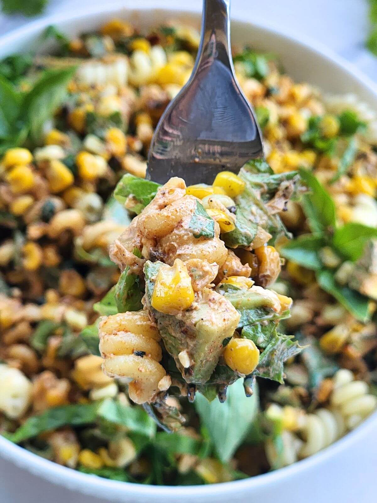 Spoonful of Mexican street corn pasta salad with pasta, charred corn, avocado, cotija cheese, herbs, and creamy chili lime dressing.