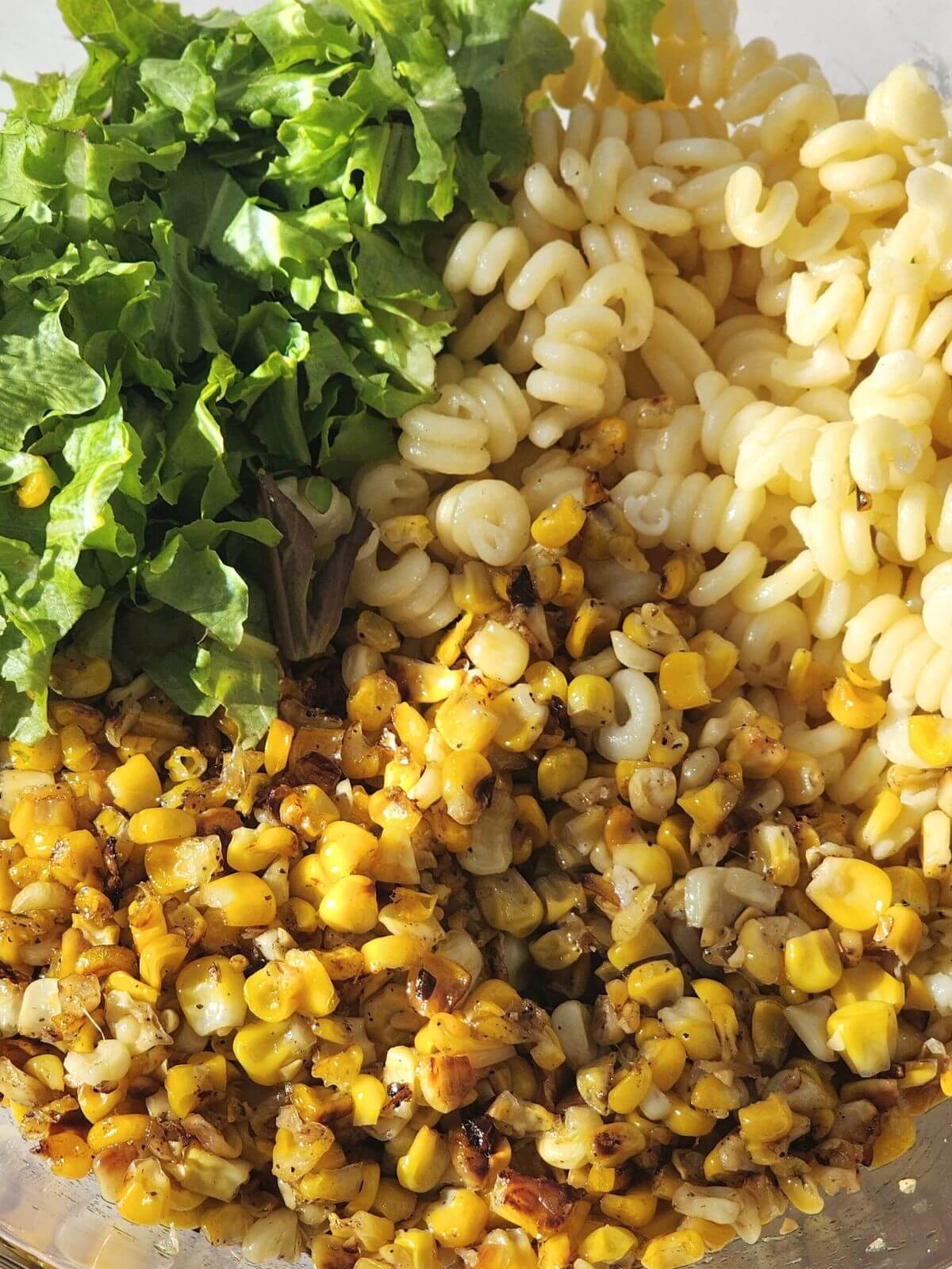 Cooked pasta, corn, and chopped lettuce in a large bowl for Mexican street corn pasta salad.