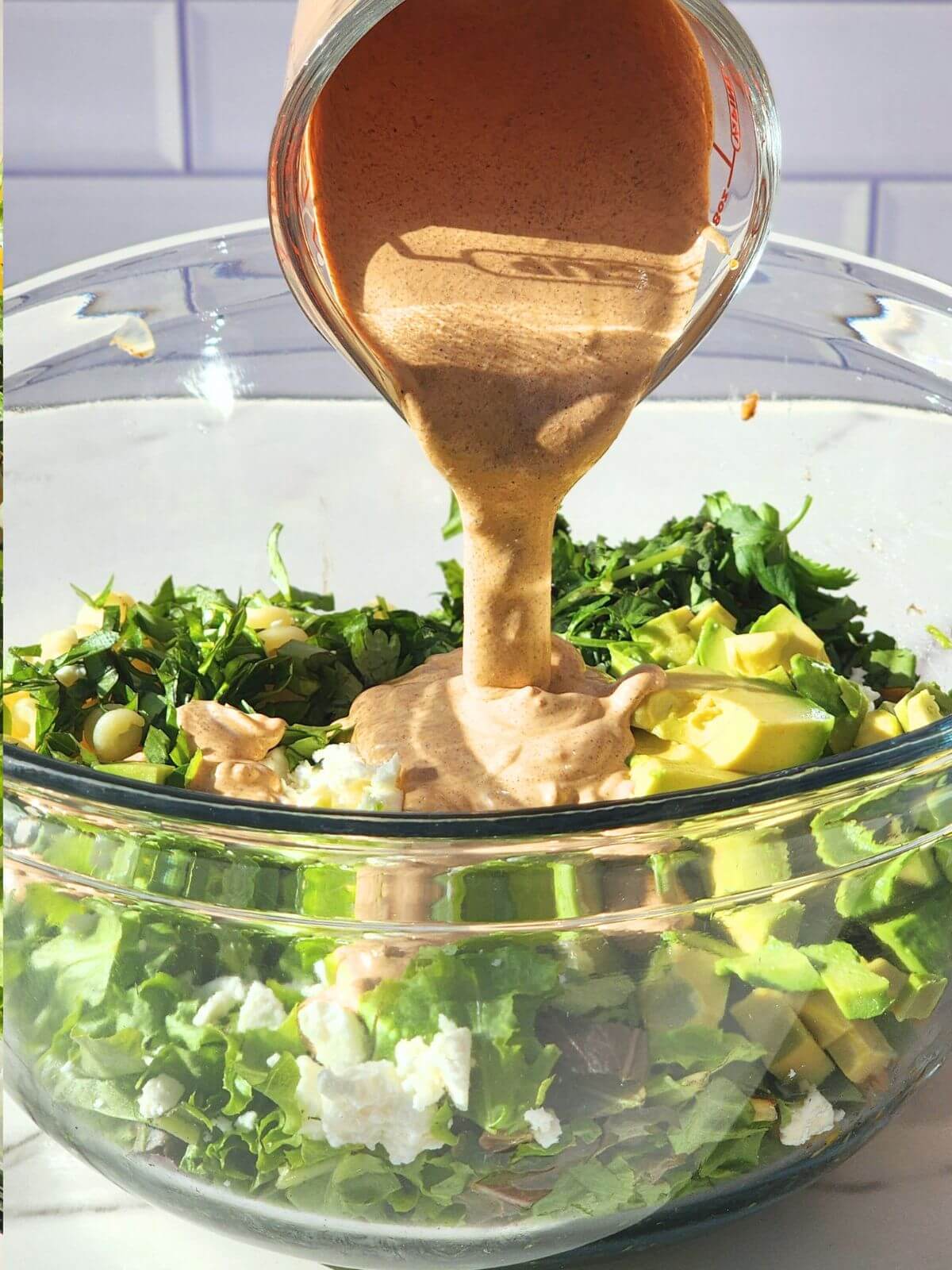 Creamy chili lime dressing being poured over Mexican street corn pasta salad with avocado, corn, cotija, and fresh herbs.