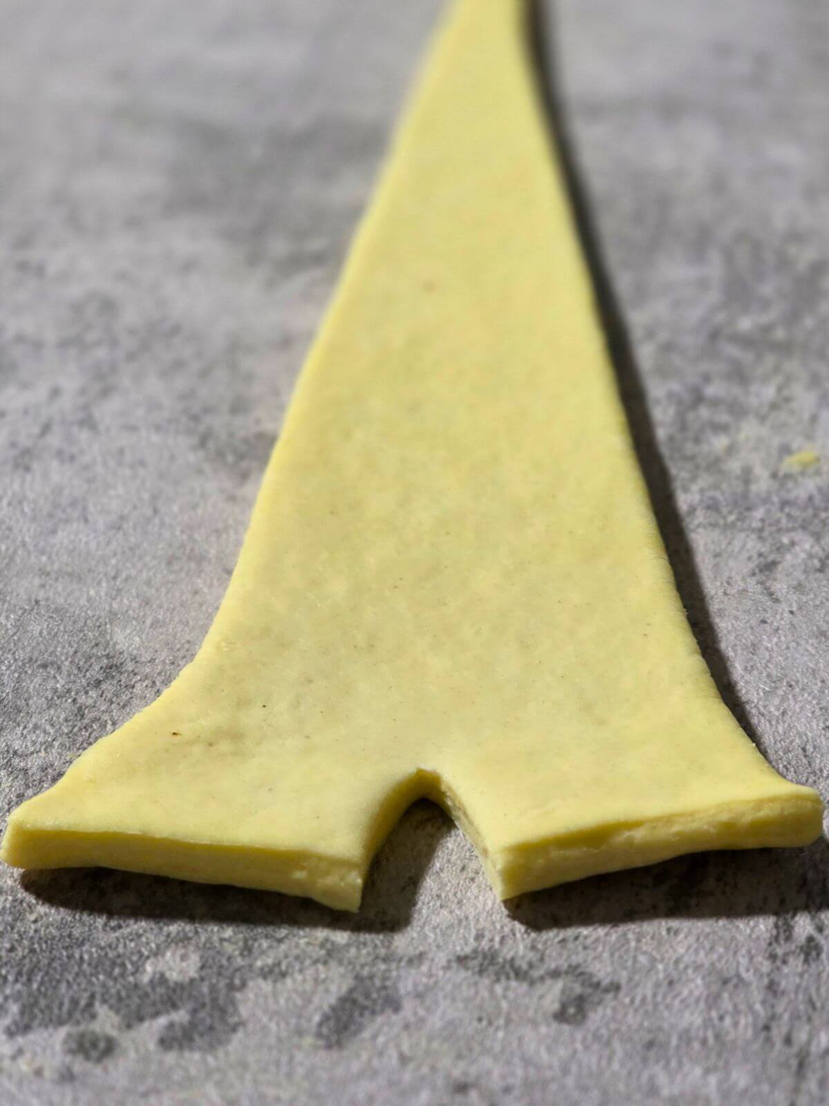 Croissant dough triangle with a small slit cut into the wide end before rolling.