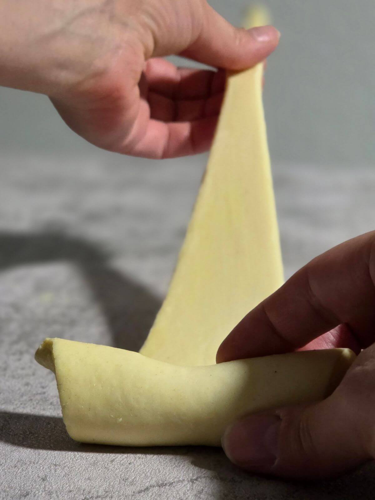 Croissant dough being rolled from the wide end toward the point.