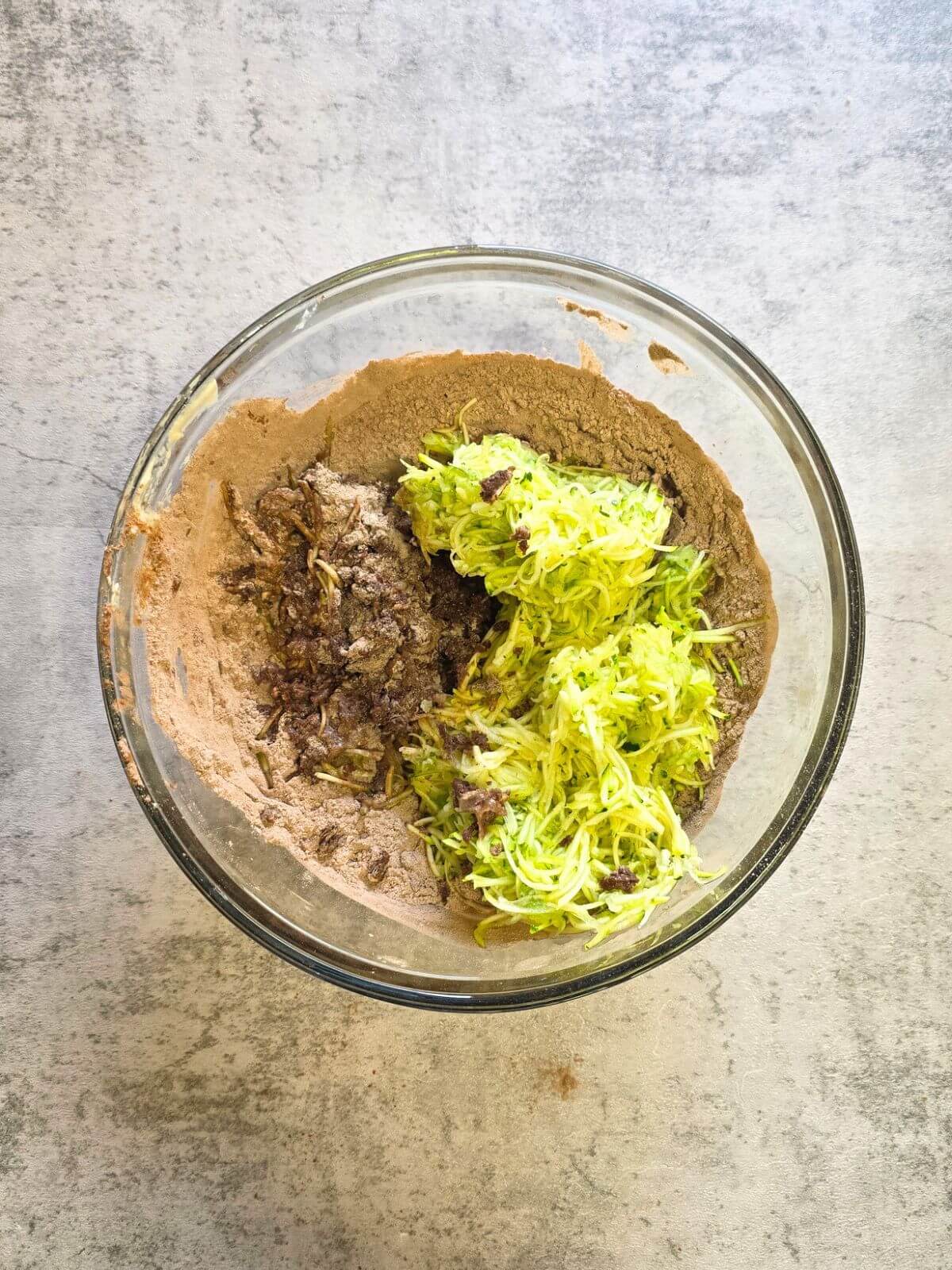 Shredded zucchini added to brownie batter ingredients in a glass mixing bowl.