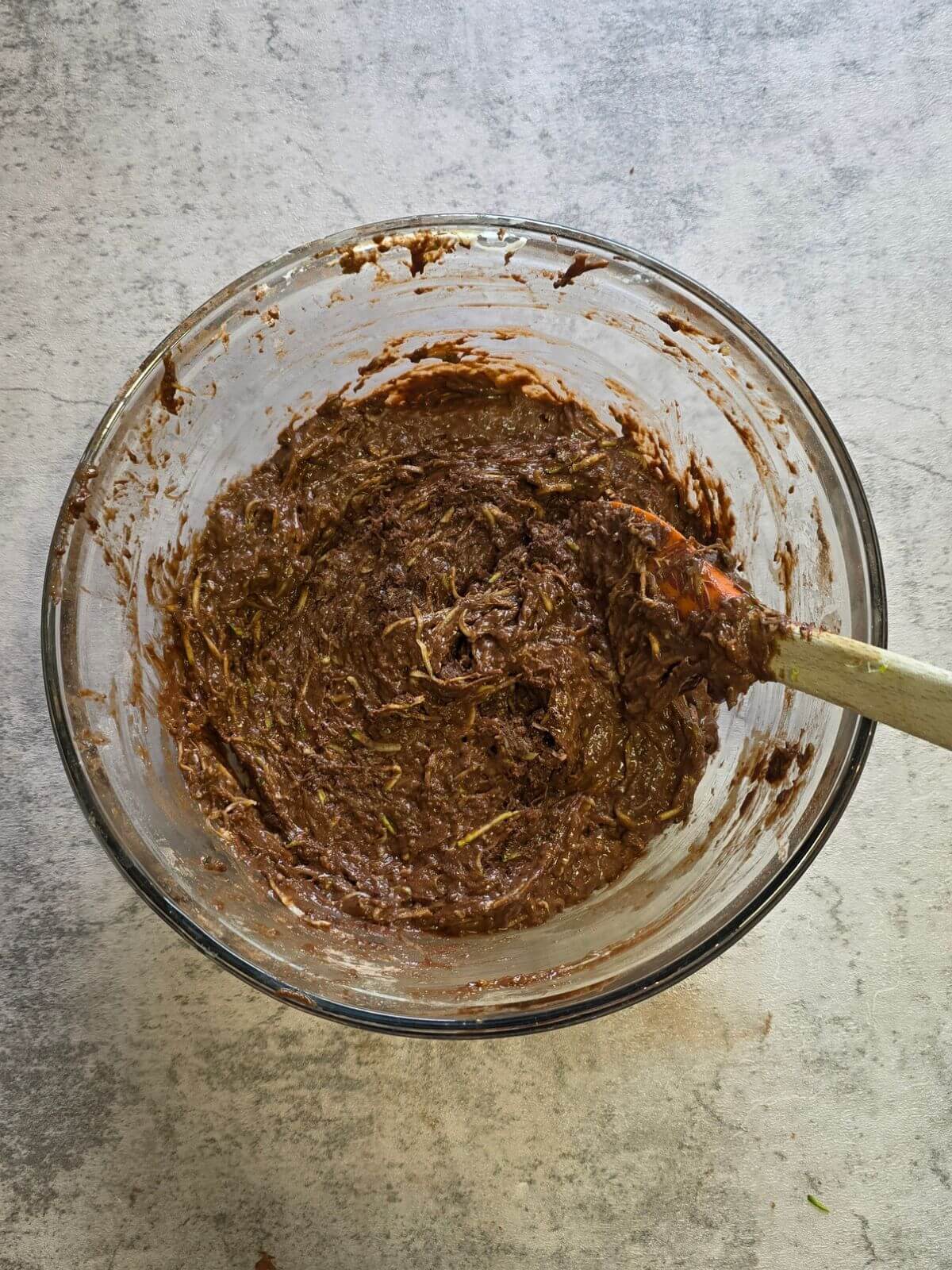 Thick chocolate zucchini brownie batter mixed together in a glass bowl.