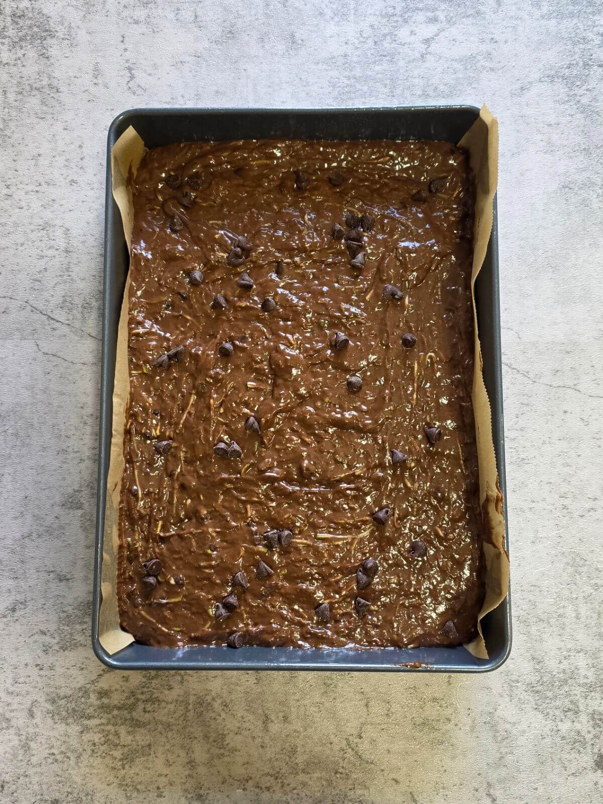 Sourdough chocolate chip zucchini brownie batter spread into a parchment lined 9x13 baking pan before baking.