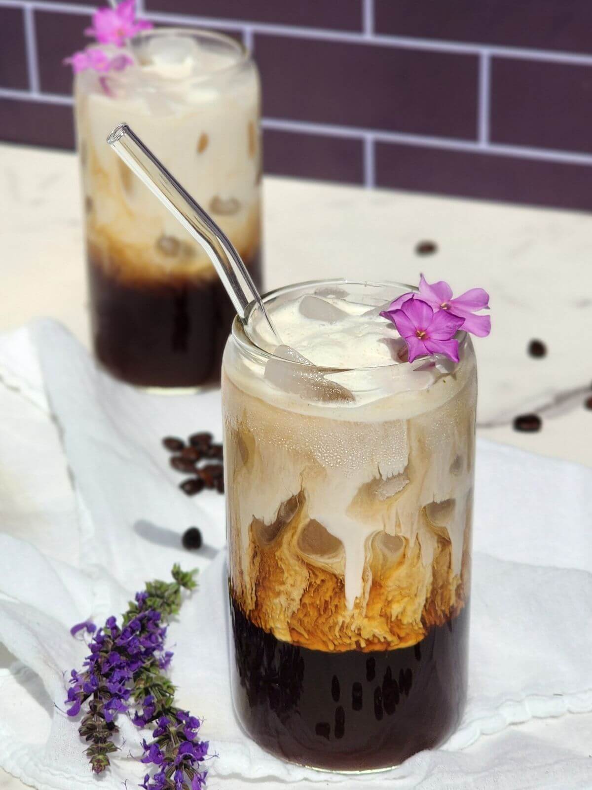 Two iced honey lavender lattes with creamy milk, espresso, ice, and purple floral garnish.