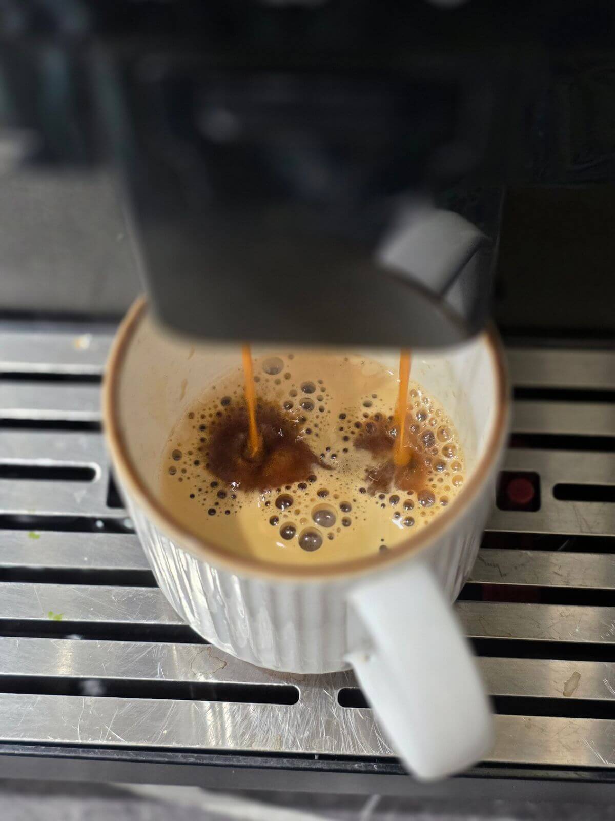 Fresh espresso shots brewing into a ceramic cup from an espresso machine.