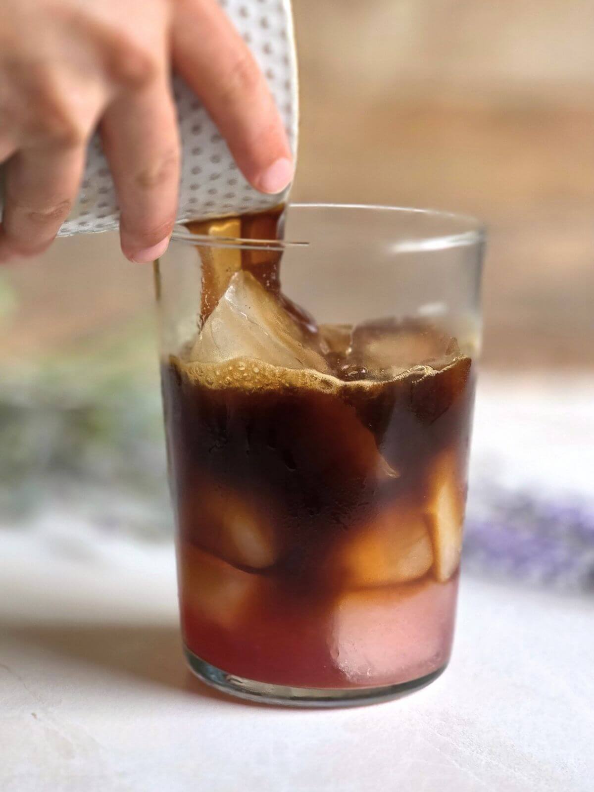Honey lavender syrup and espresso being poured over ice in a clear glass to make an iced honey lavender latte.