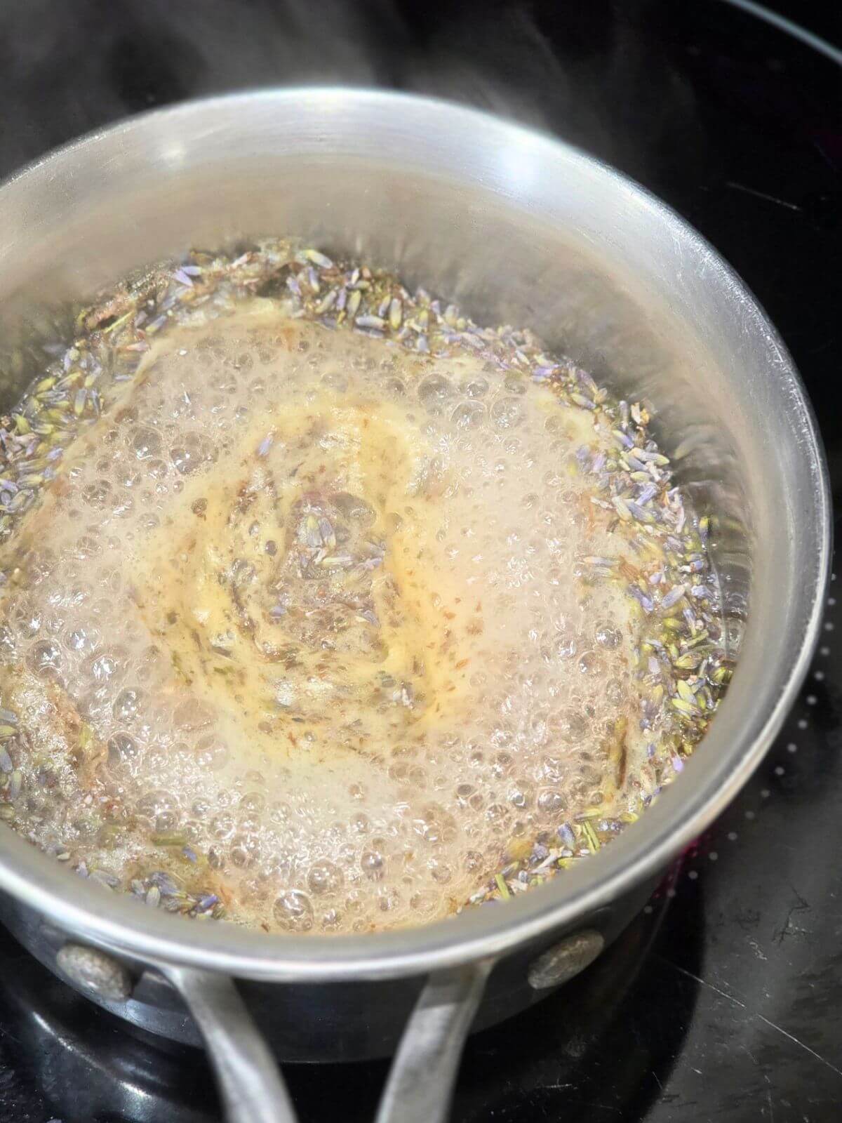 Honey lavender syrup simmering with dried culinary lavender in a small saucepan.