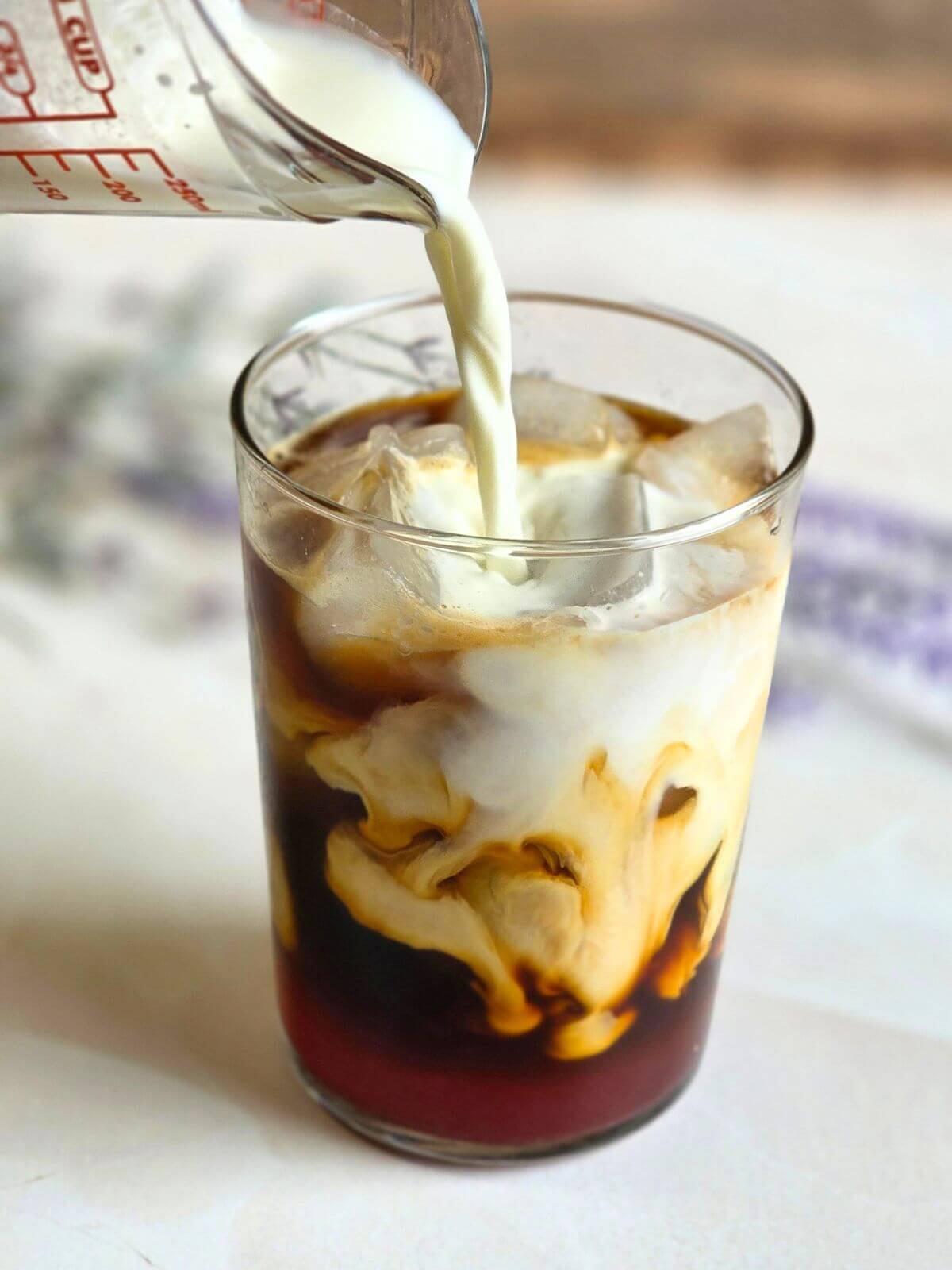 Milk being poured into an iced honey lavender latte over espresso and ice.