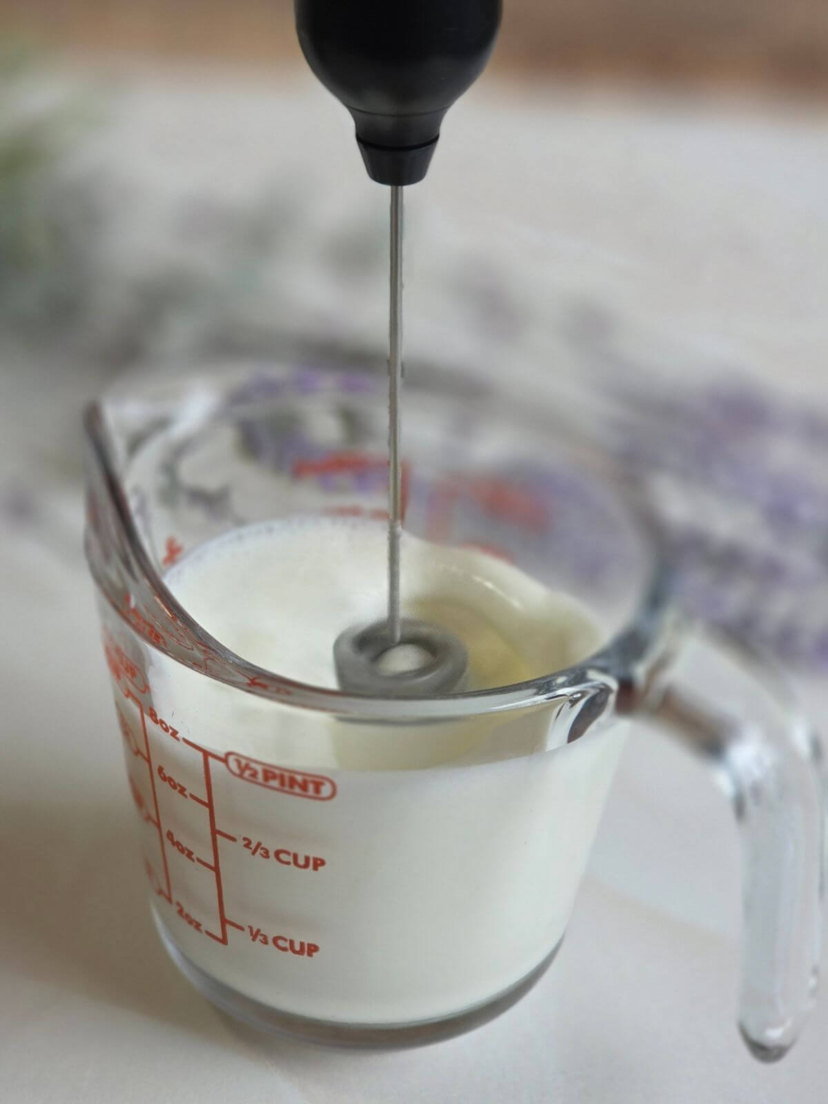 Milk being frothed in a glass measuring cup with a handheld milk frother.